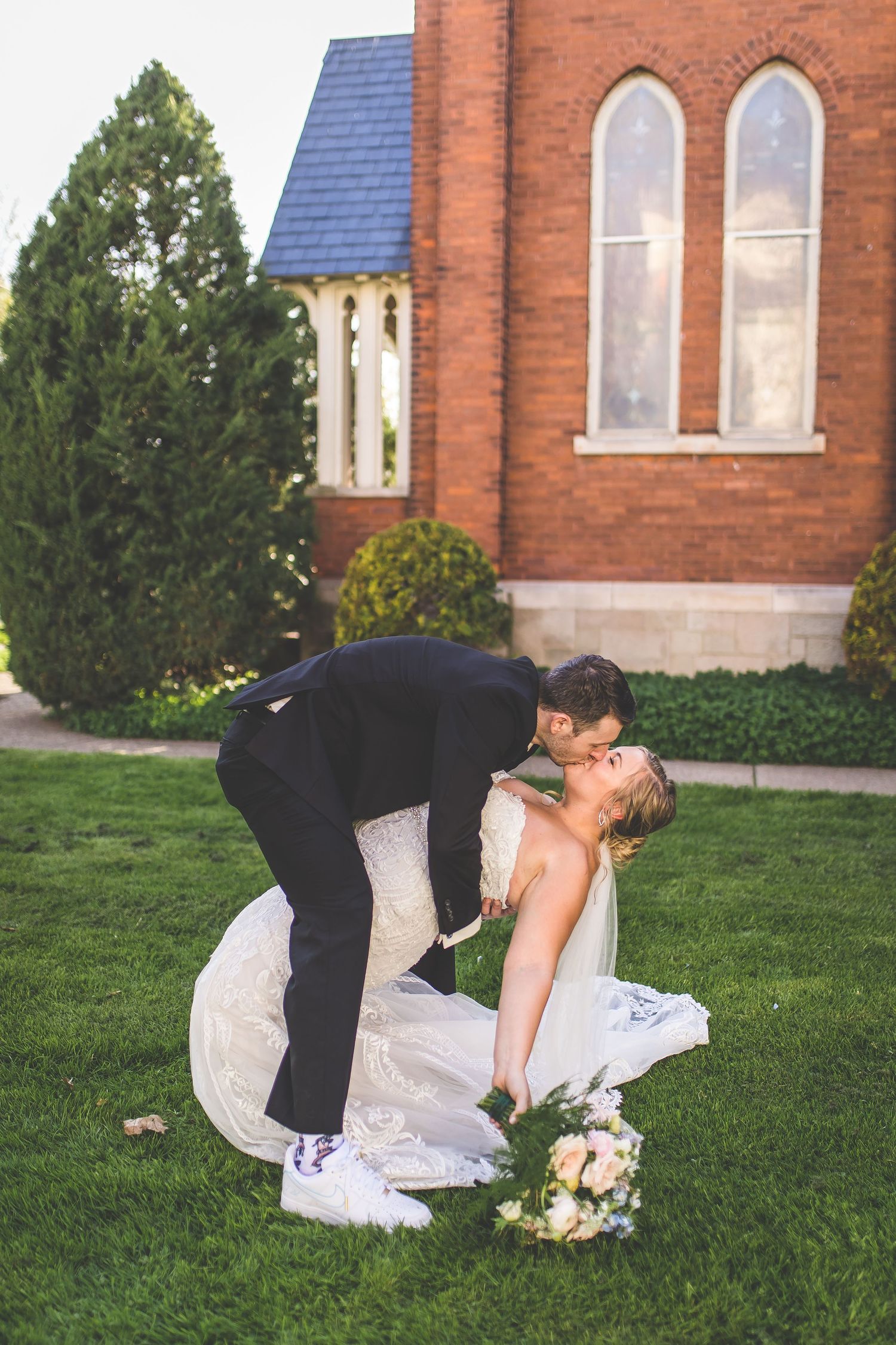 Newlyweds share intimate dip pose on green lawn in front of historic church.