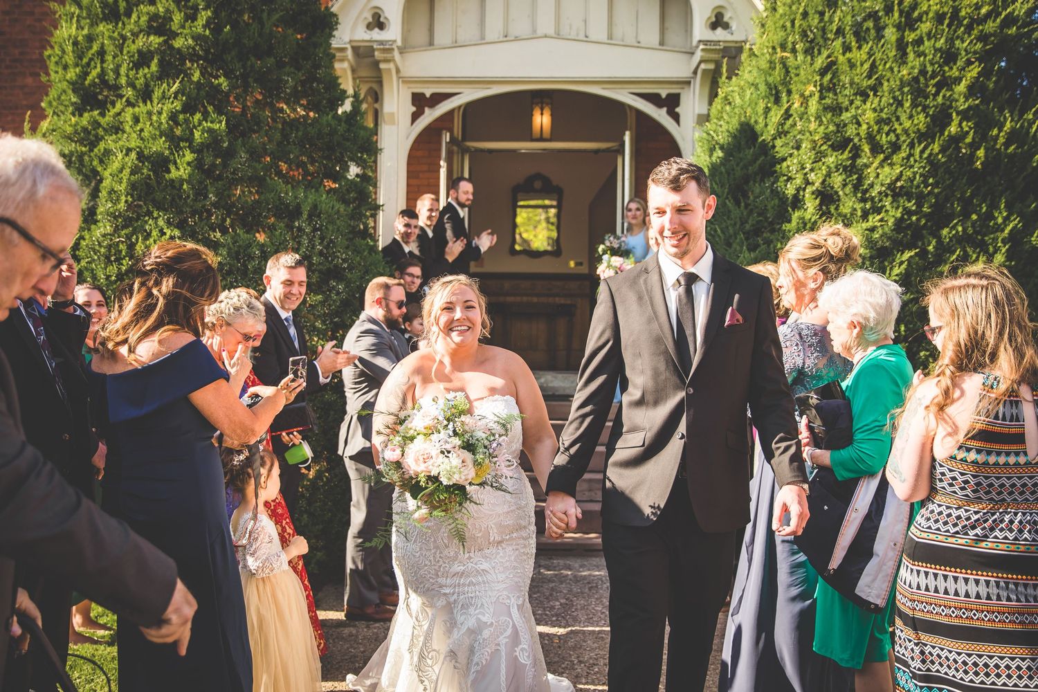 Joyful outdoor wedding reception with guests mingling under architectural details.