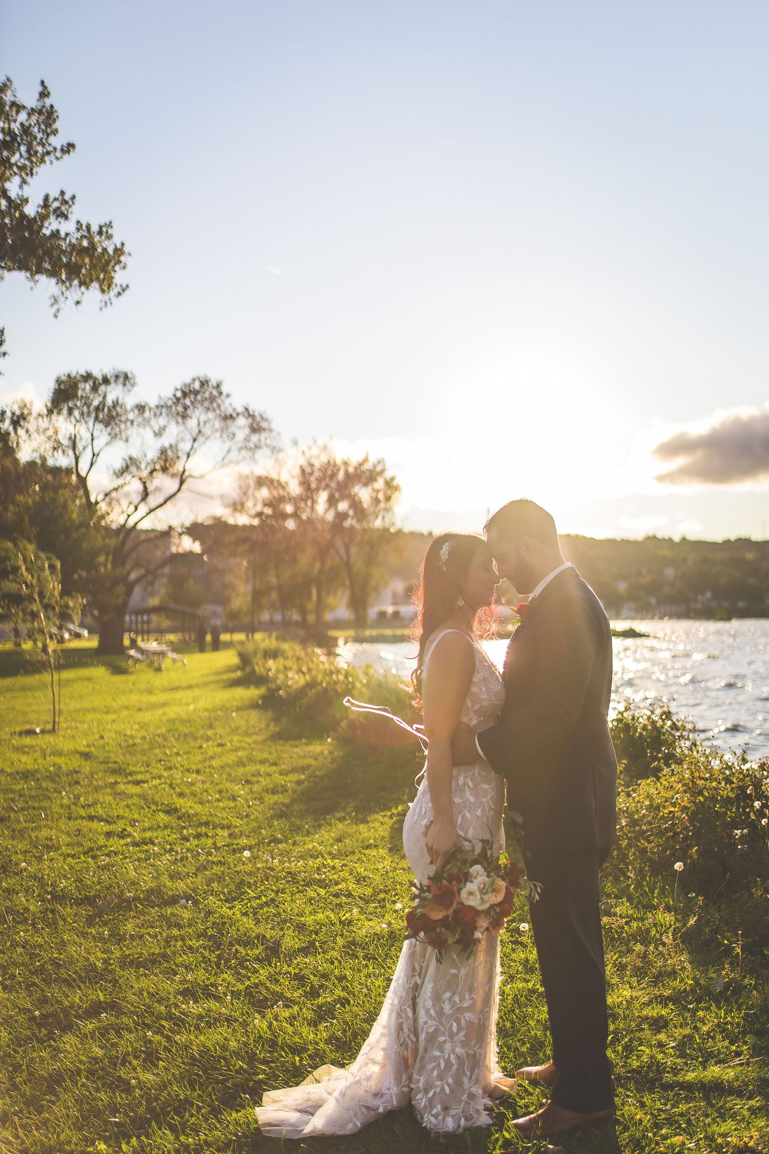 Couple shares romantic sunset moment by waterfront with golden light streaming through trees.