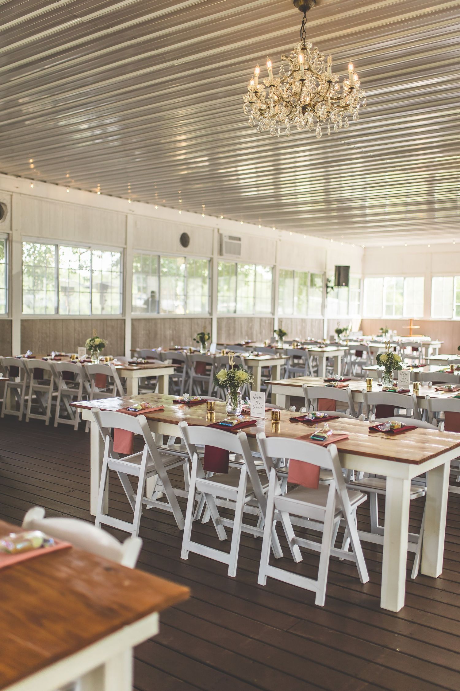 Wedding reception venue with white tables, folding chairs, and crystal chandelier in an elegant covered porch.