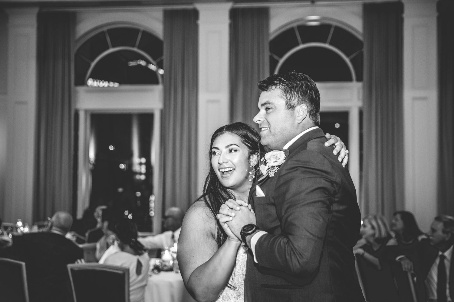 Black and white photo of a couple dancing at their wedding reception in a grand ballroom.