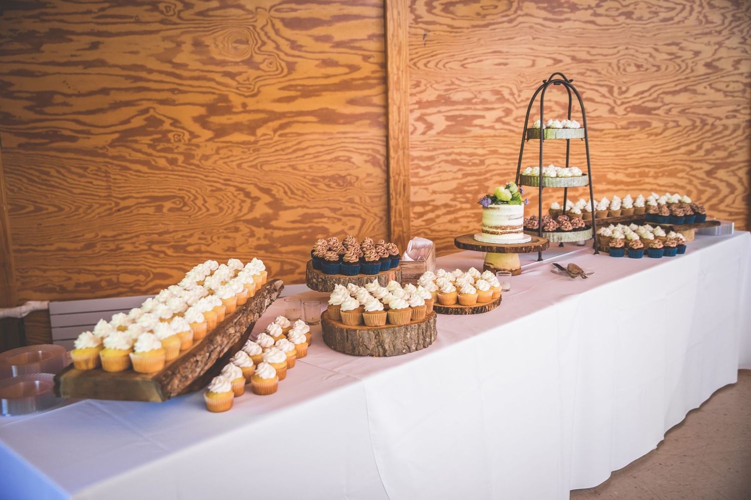 A dessert table with cupcakes and treats arranged on a white tablecloth against wooden walls.