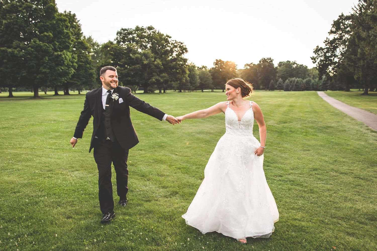 Newlyweds walking hand in hand on a scenic golf course path at sunset.