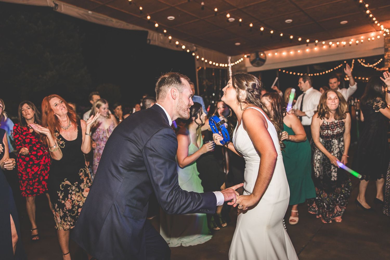 Energetic dancing at wedding reception with string lights creating warm ambiance.