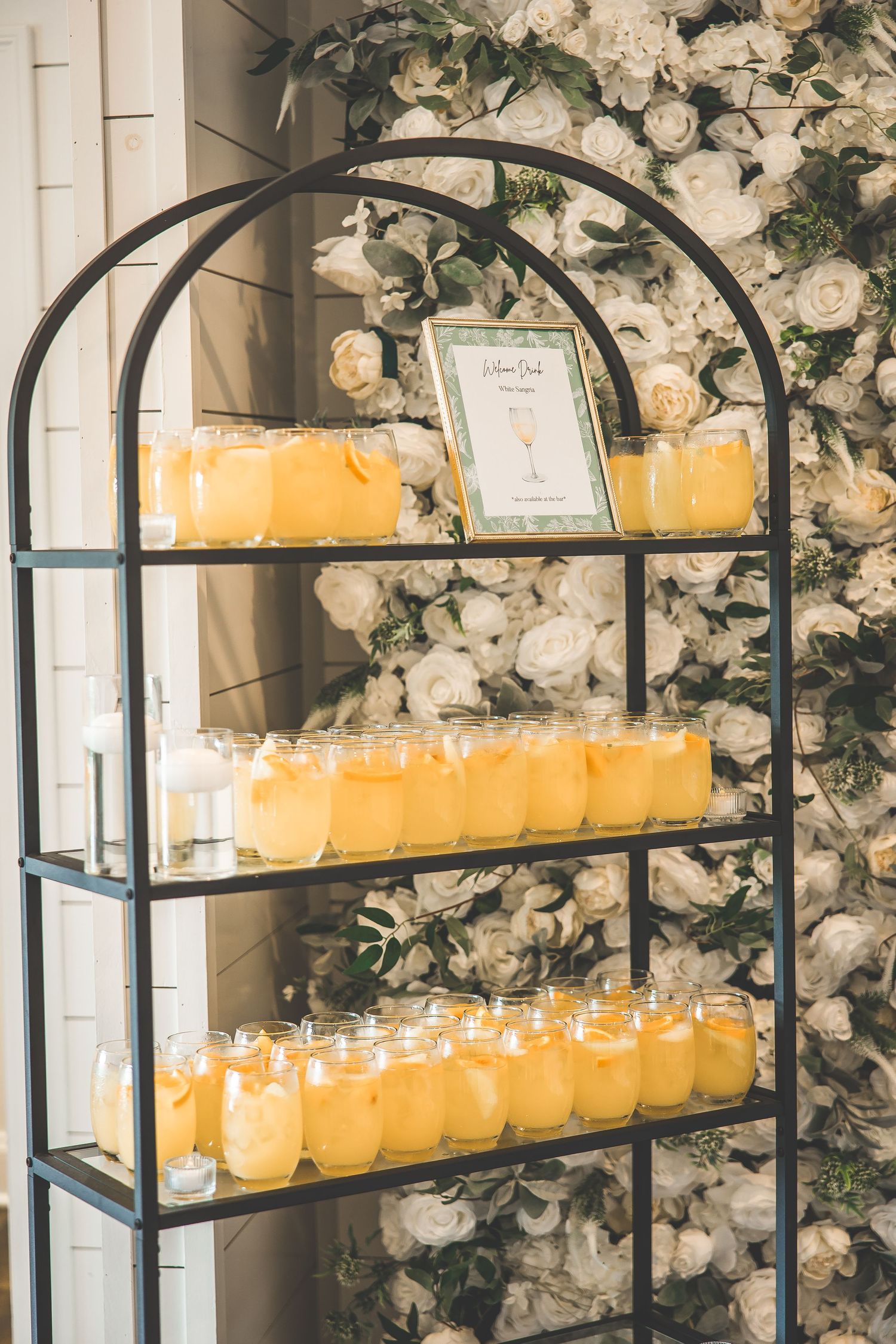 Display of yellow candles on tiered black metal shelves with white floral backdrop.