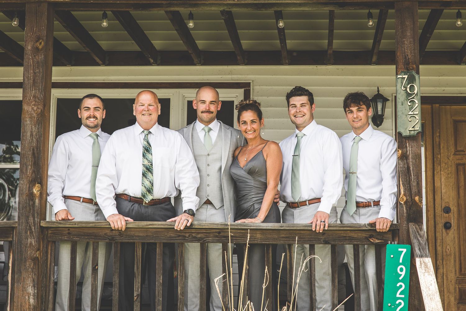 Groomsmen in light gray suits pose on rustic wooden porch.