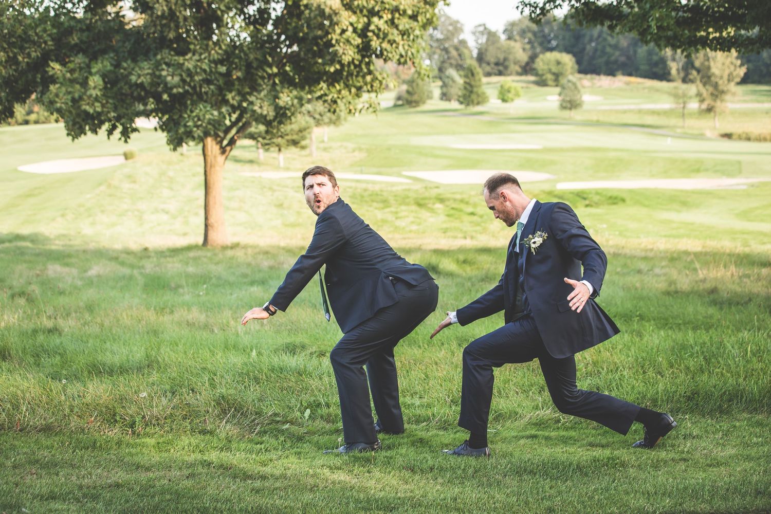 Two groomsmen strike funny poses on golf course during wedding photos.