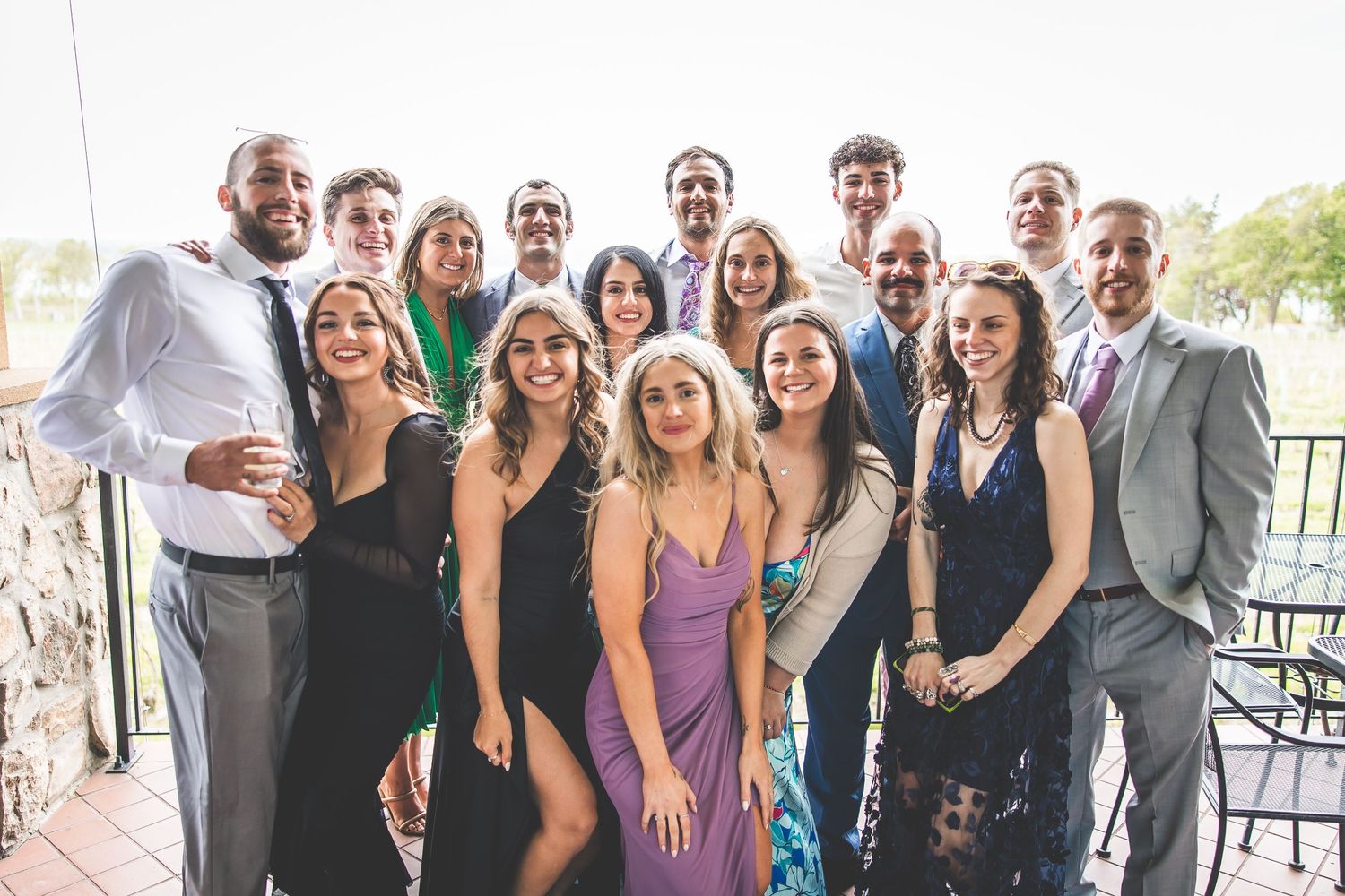 Wedding celebration group photo with guests in formal attire on an outdoor patio.