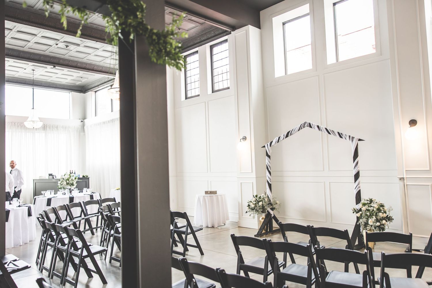 Spacious wedding venue with industrial ceiling, large windows, and modern black chairs.