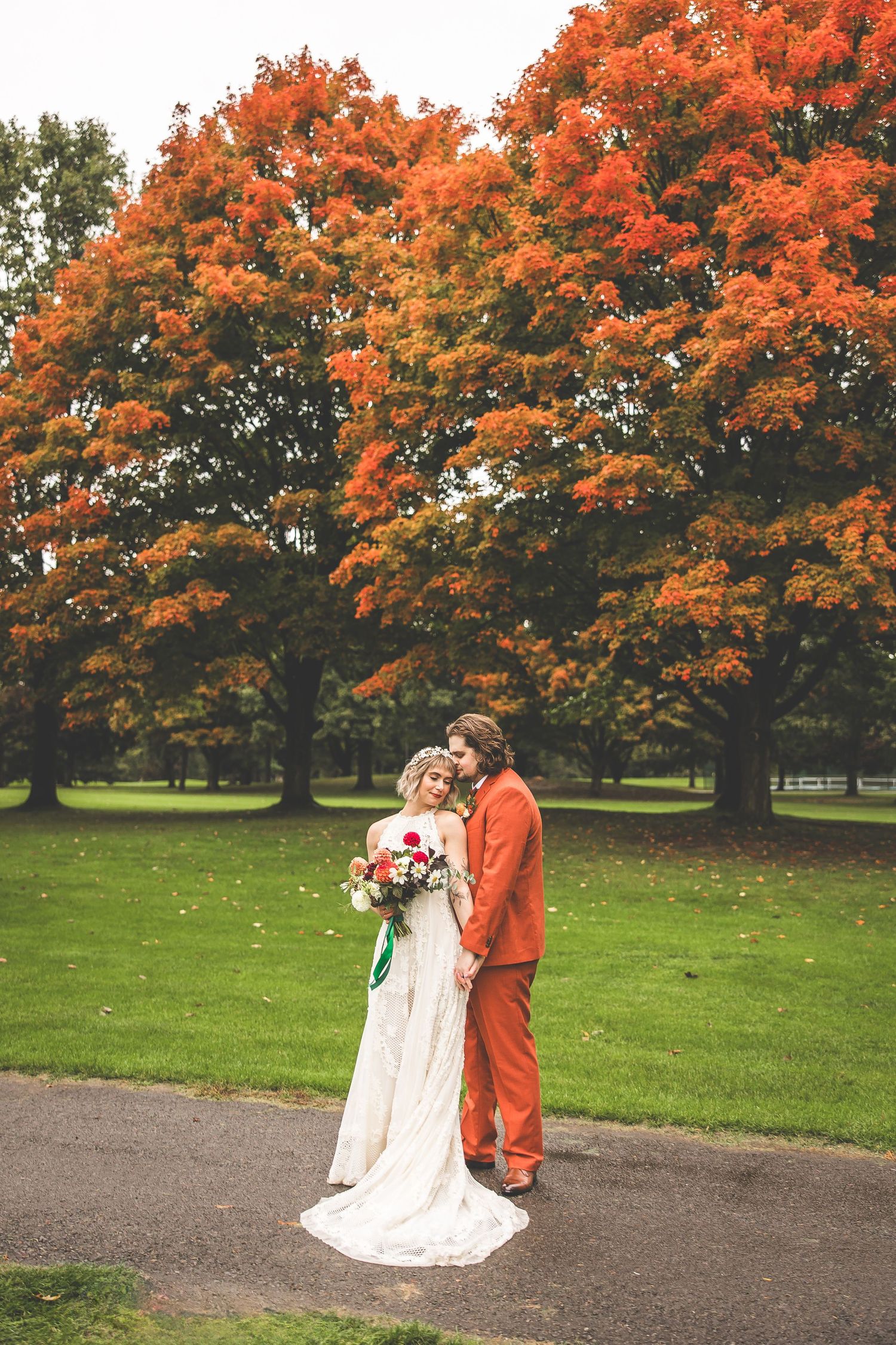 Newlyweds stand beneath vibrant orange maple trees on their autumn wedding day.