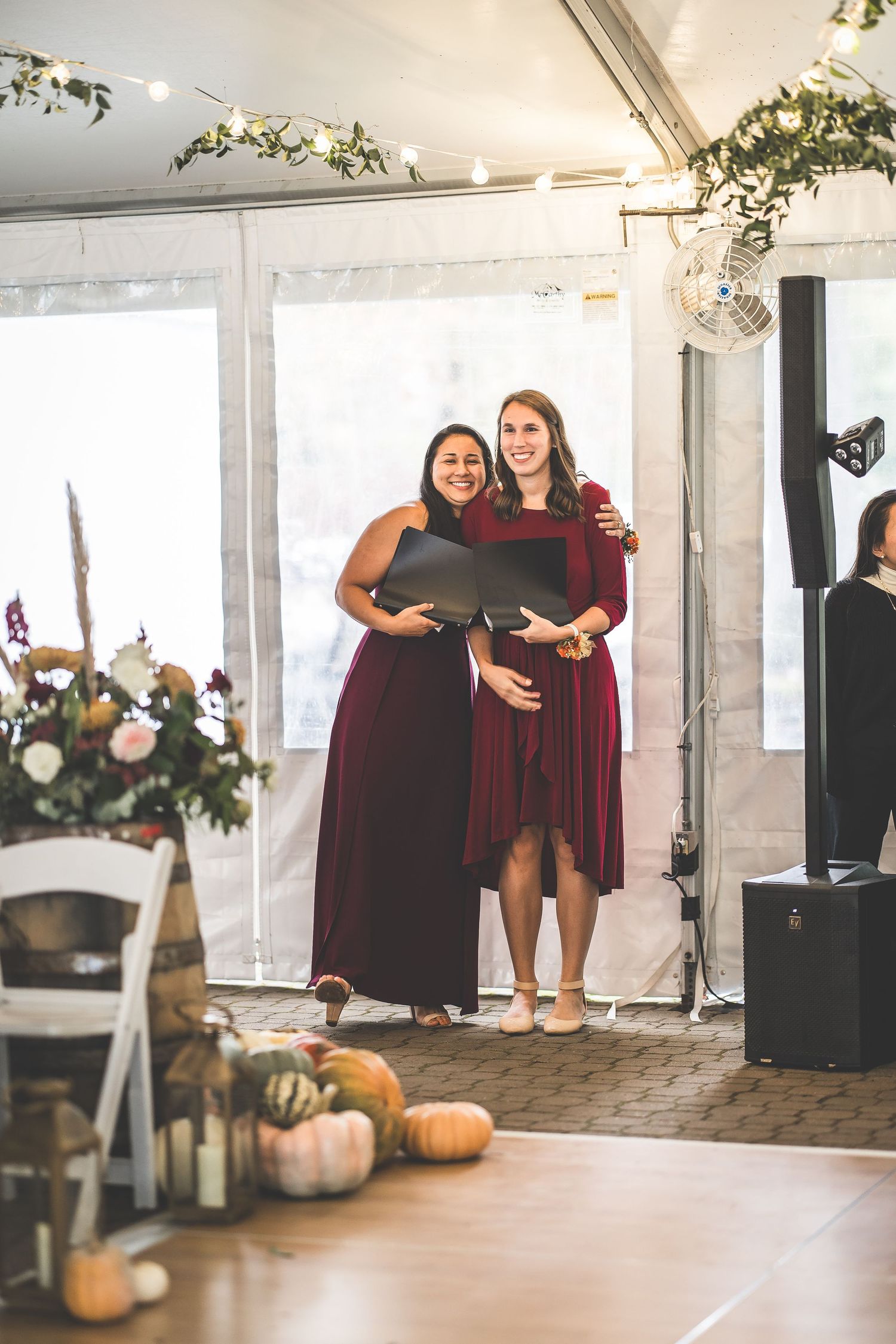 Two people share a joyful moment in a bright indoor venue decorated with pumpkins and greenery.