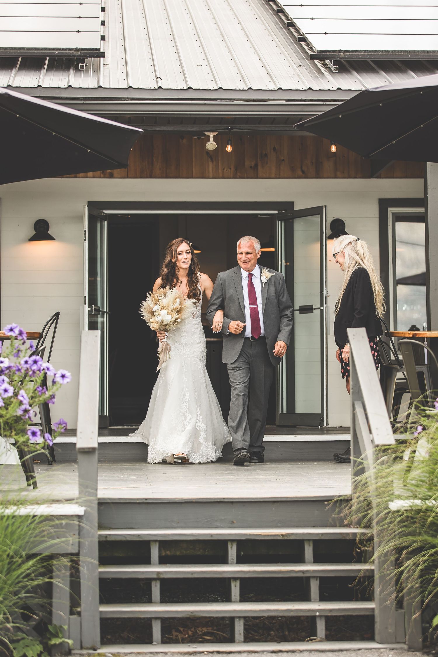 Wedding ceremony on a modern deck with white chairs and rustic decor overlooking a scenic view.