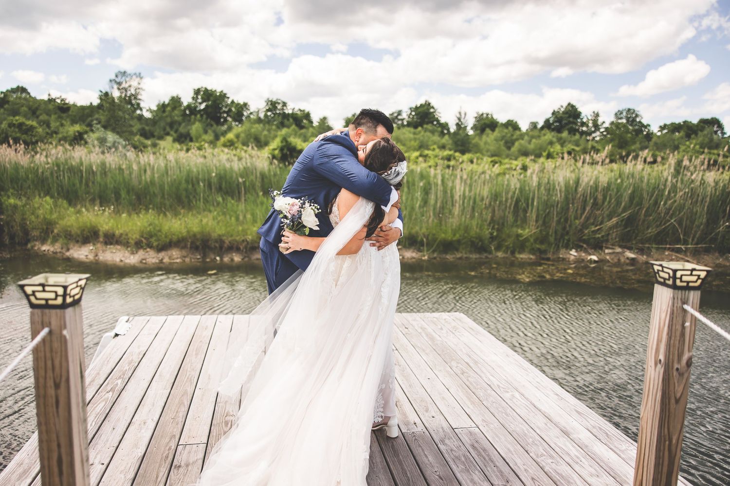 Newlyweds share intimate moments on a rustic dock surrounded by natural scenery.