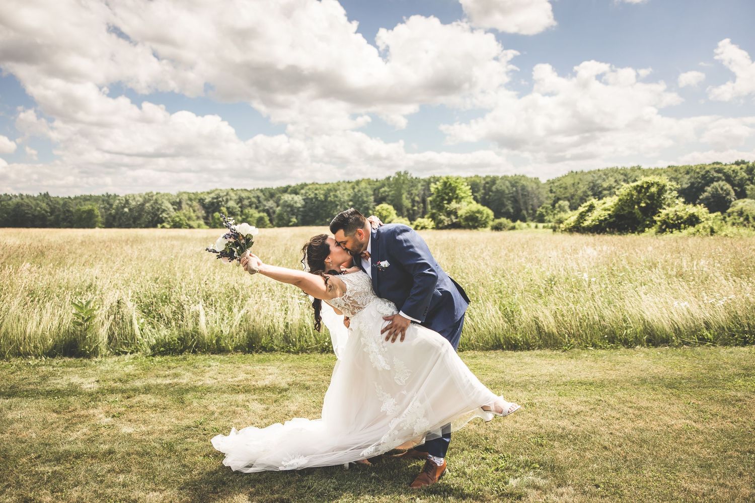 Wedding couple posing in scenic meadow with dramatic cloudy sky backdrop.