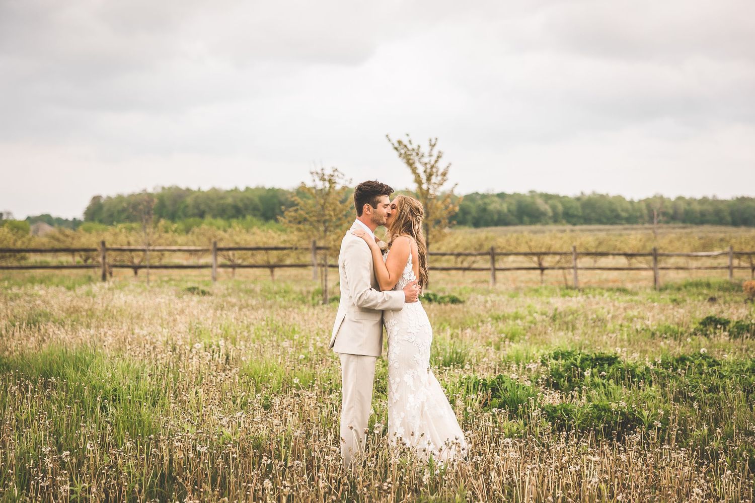 Newlyweds share an intimate moment in a rustic field with tall grass and wildflowers.