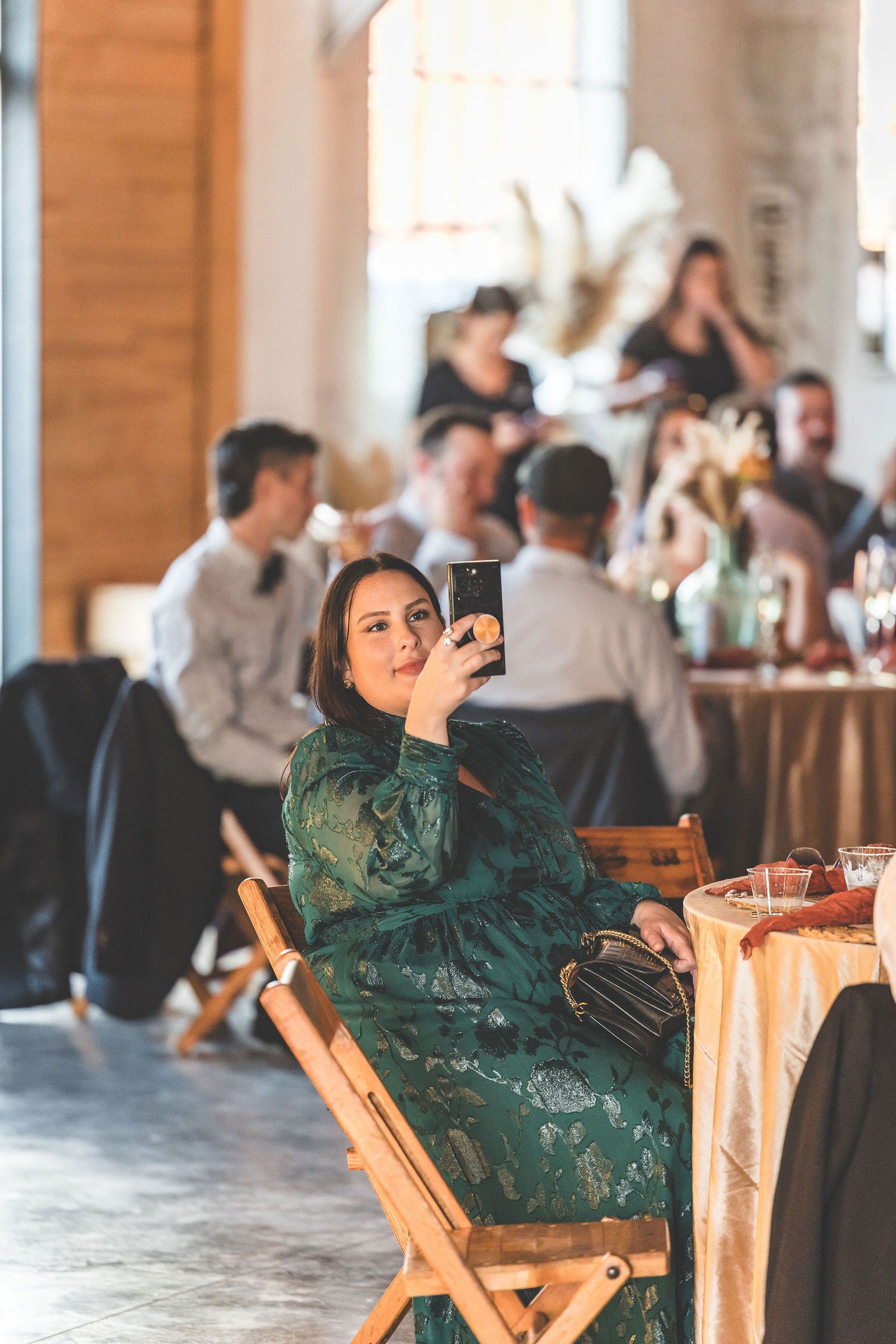 Guest in emerald dress relaxes at rustic wedding reception venue.