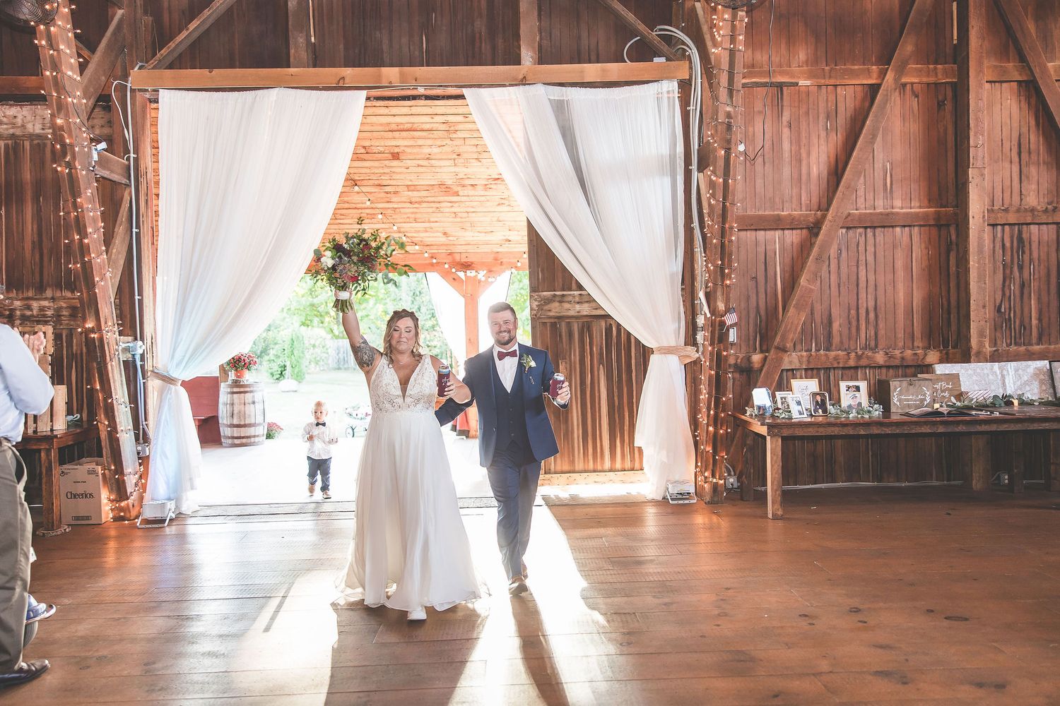 Wedding celebration in a beautifully decorated barn venue with white fabric draping and natural light streaming in.