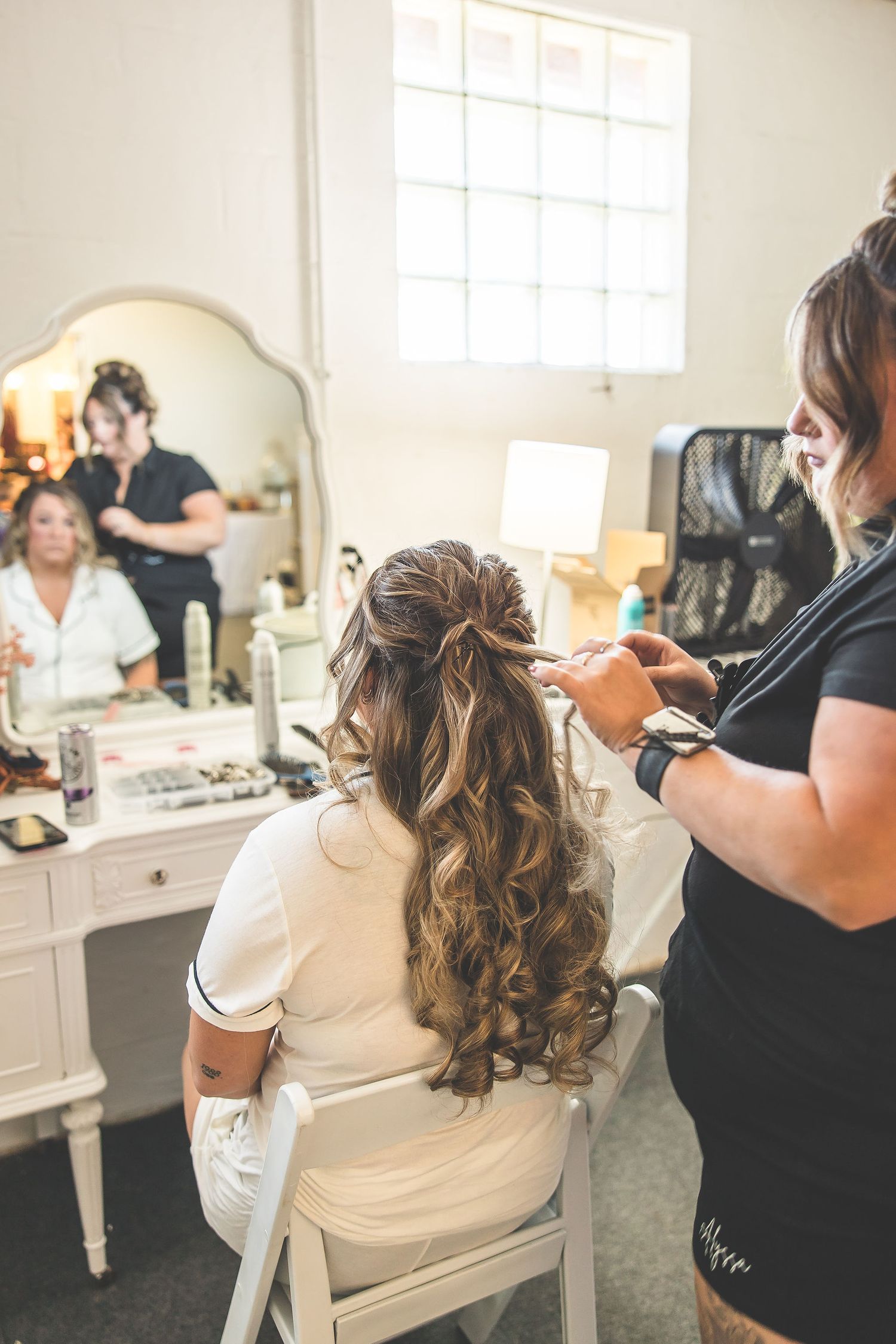 Wedding day hair styling preparation in a bright white dressing room with mirrors.