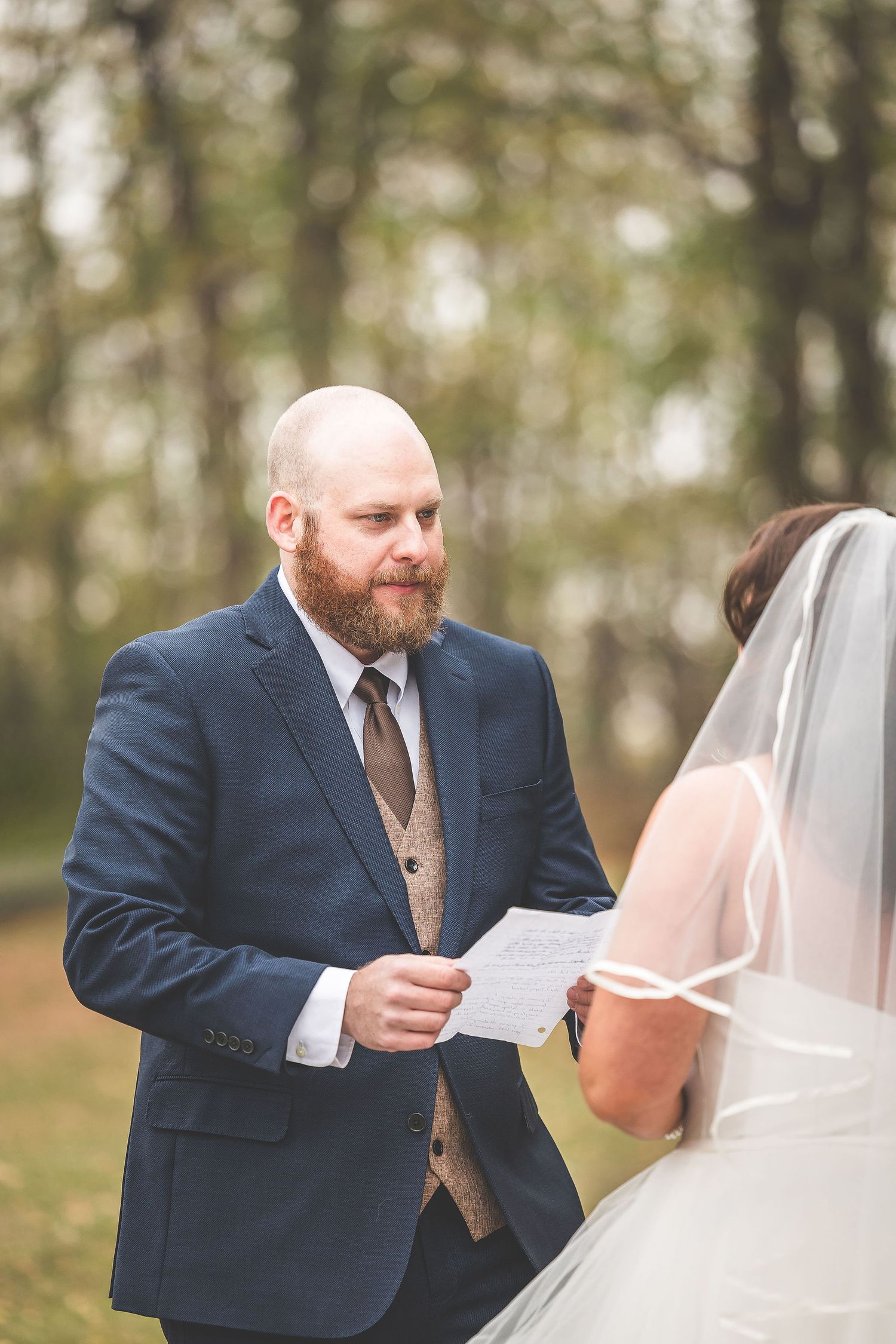 A groom reads from a paper during an intimate forest wedding ceremony.