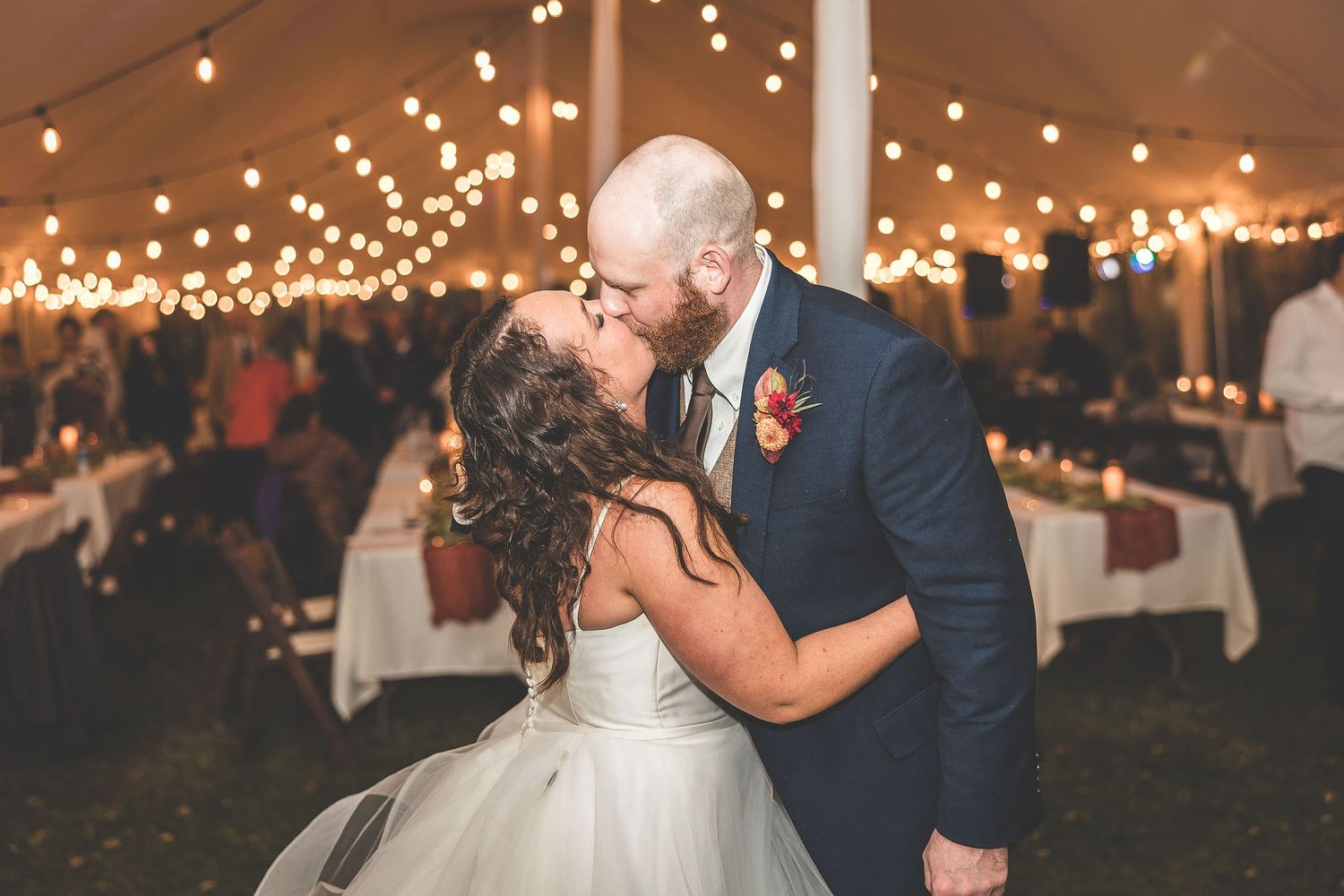 Romantic wedding dance under warm string lights in an elegant tent setting.