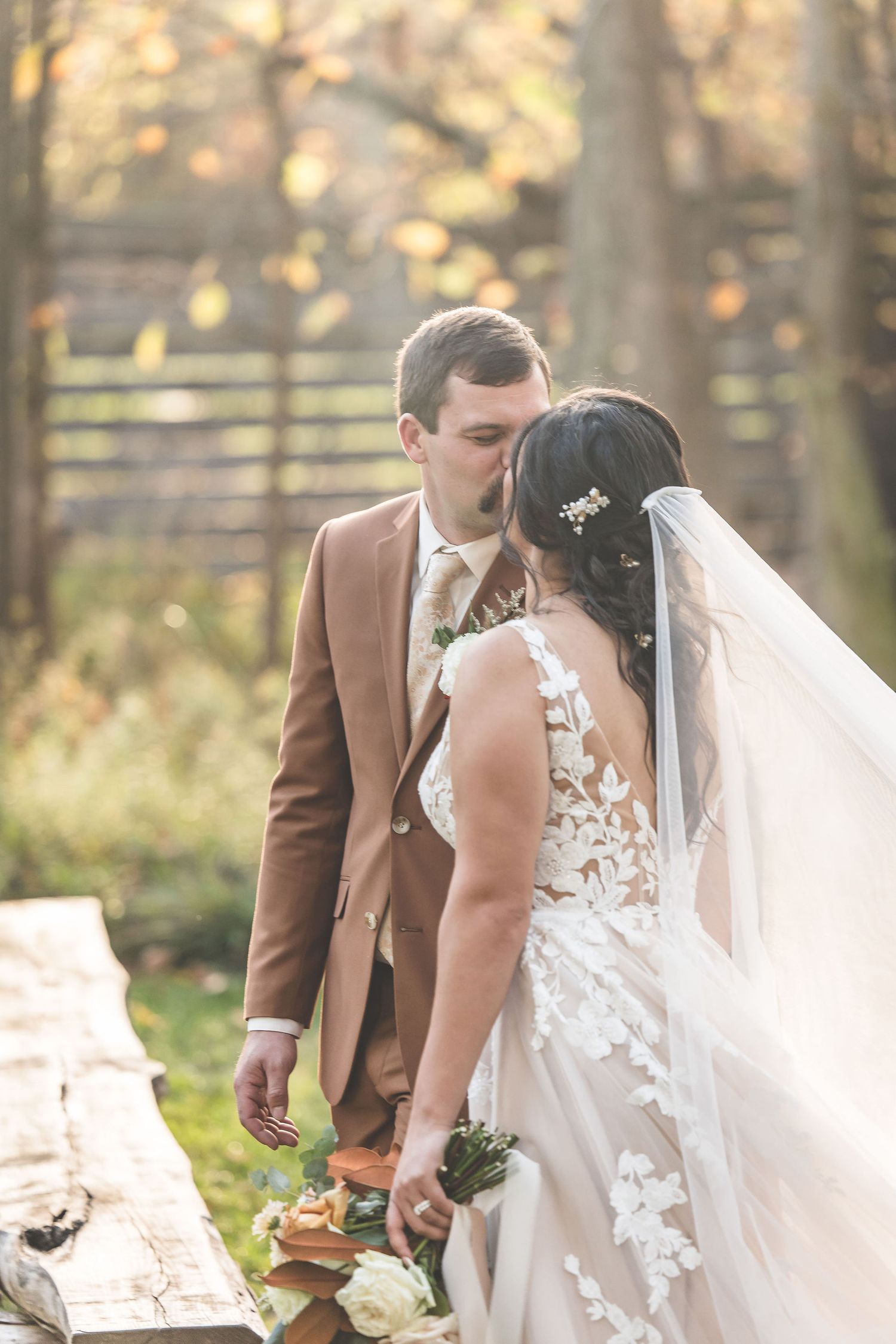 Elegant wedding couple shares an intimate moment in a sun-dappled autumn forest.