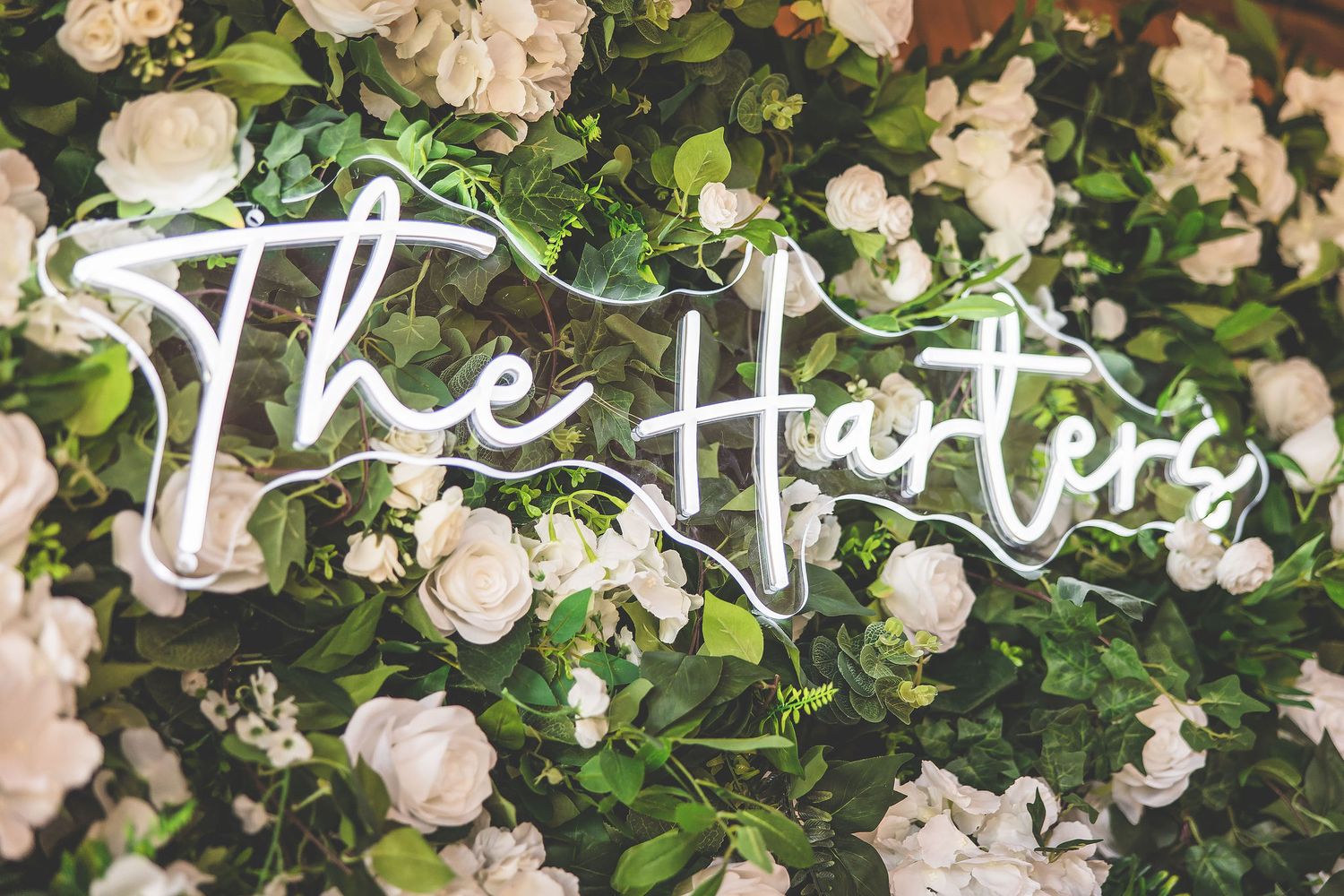 Elegant neon sign reading 'The Harters' mounted on white floral wall backdrop.