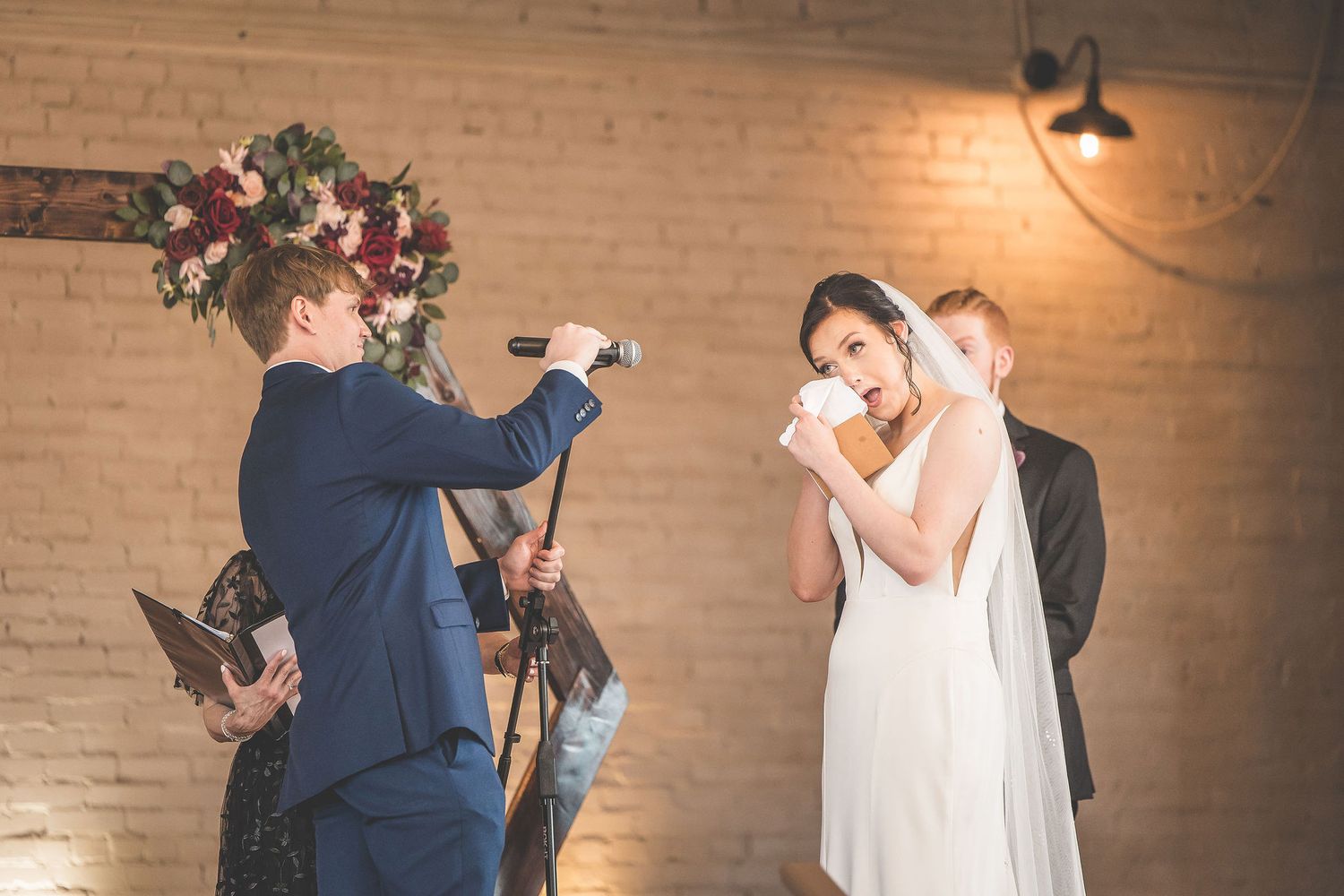 Wedding ceremony in progress with wooden geometric backdrop and floral decorations.