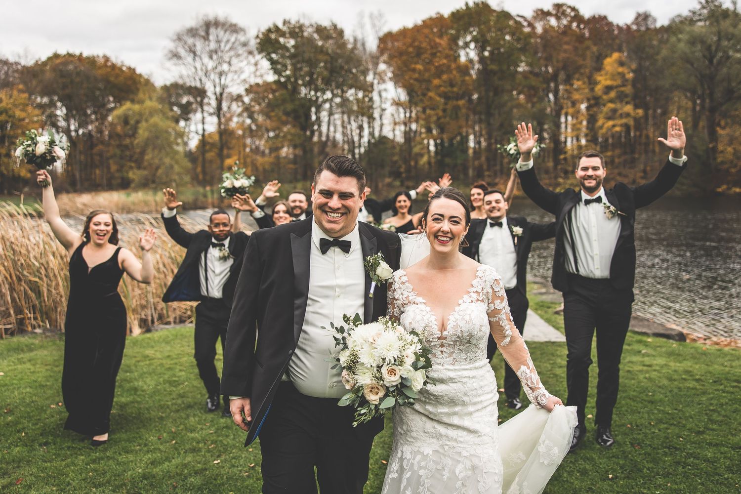 Wedding party enjoying candid moments outdoors with autumn trees in background.