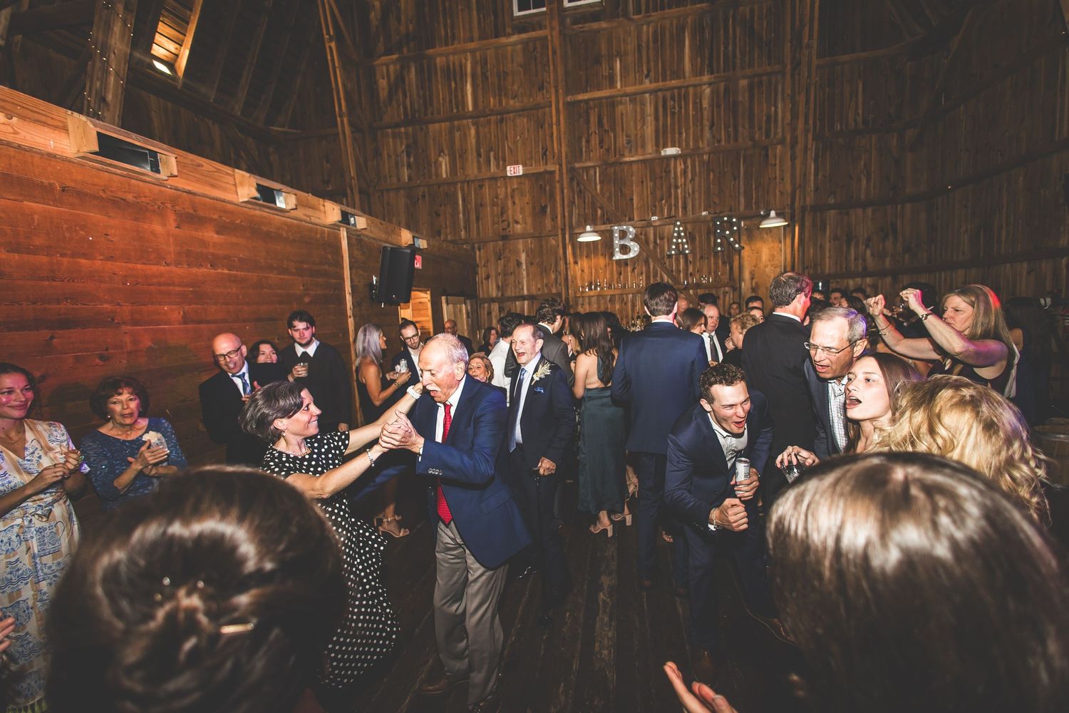 Wide shot of wedding reception dance floor with guests celebrating in barn setting.