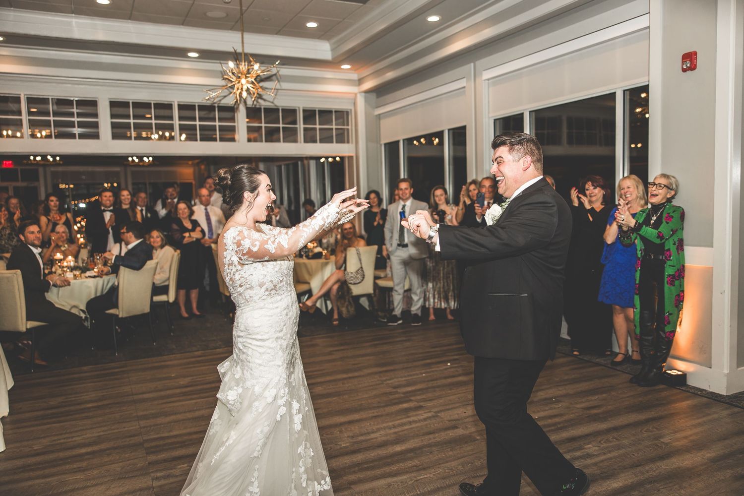 Wedding couple dancing energetically on a wooden dance floor surrounded by guests at their reception.