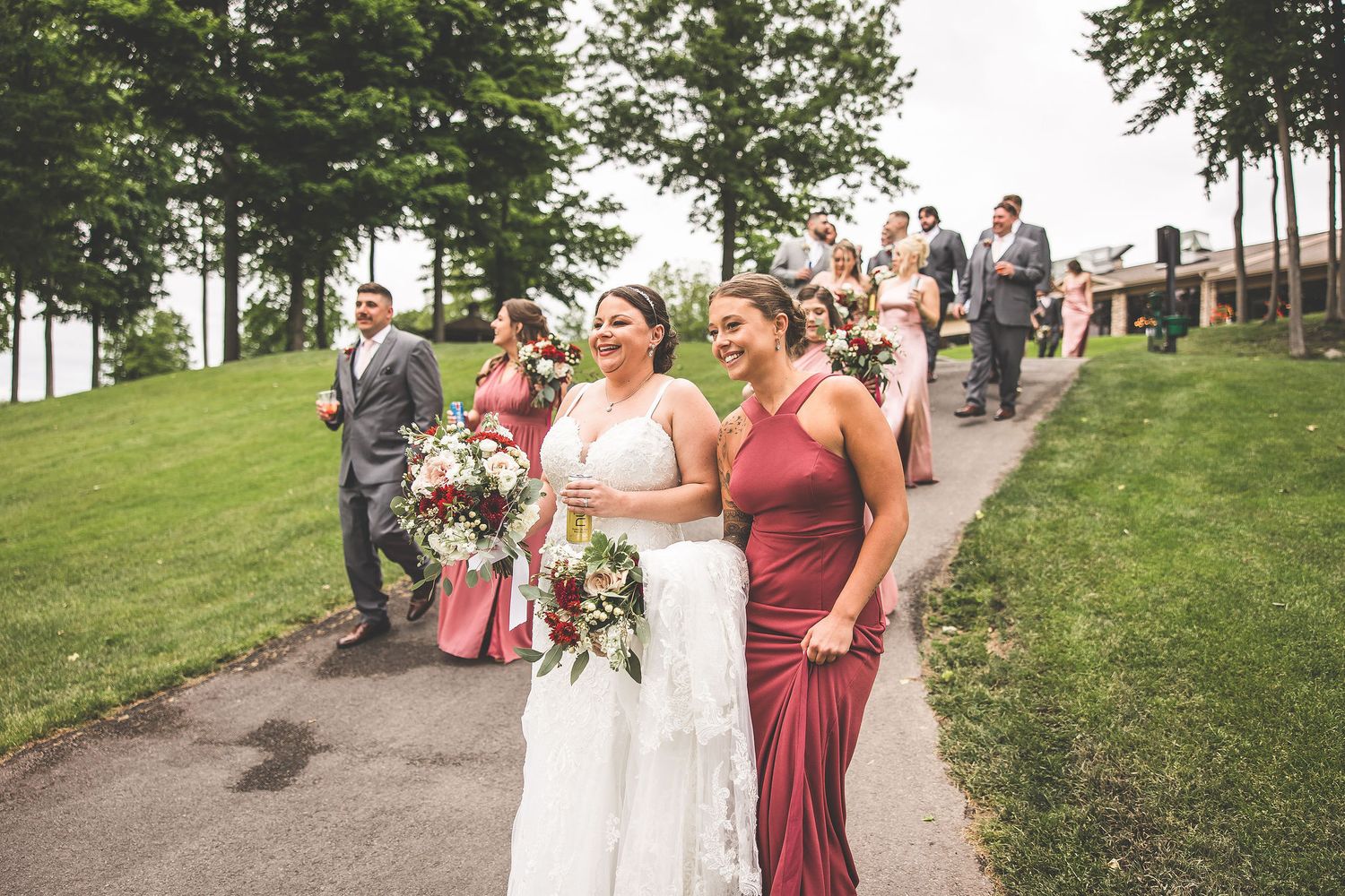 Wedding party and guests mingle on grassy hillside during outdoor celebration.