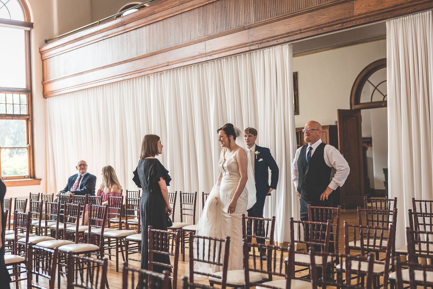 Wedding ceremony setup with white draping and wooden chairs in an elegant indoor venue.