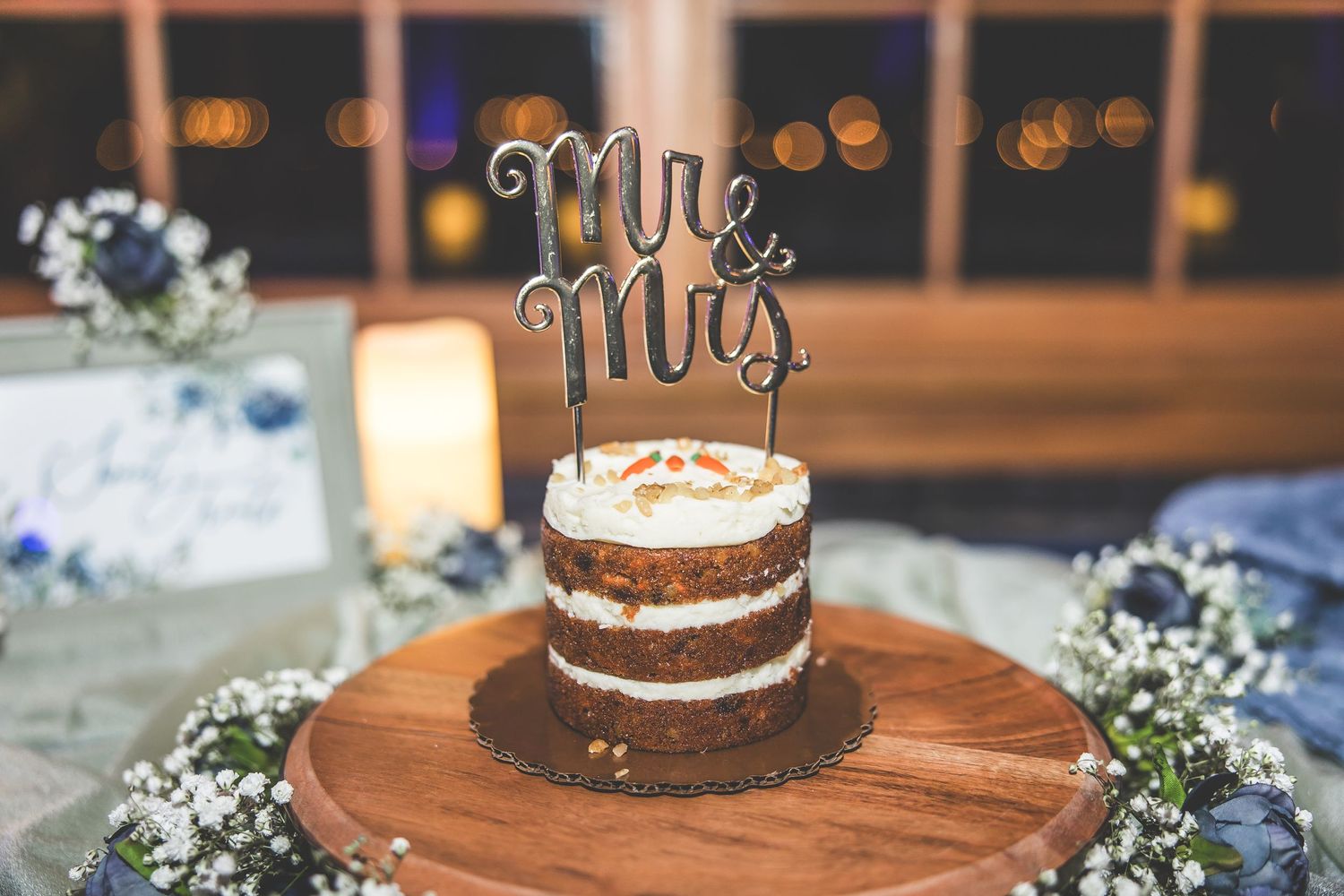 Wedding cake display featuring Mr and Mrs toppers on a wooden stand with delicate floral accents.
