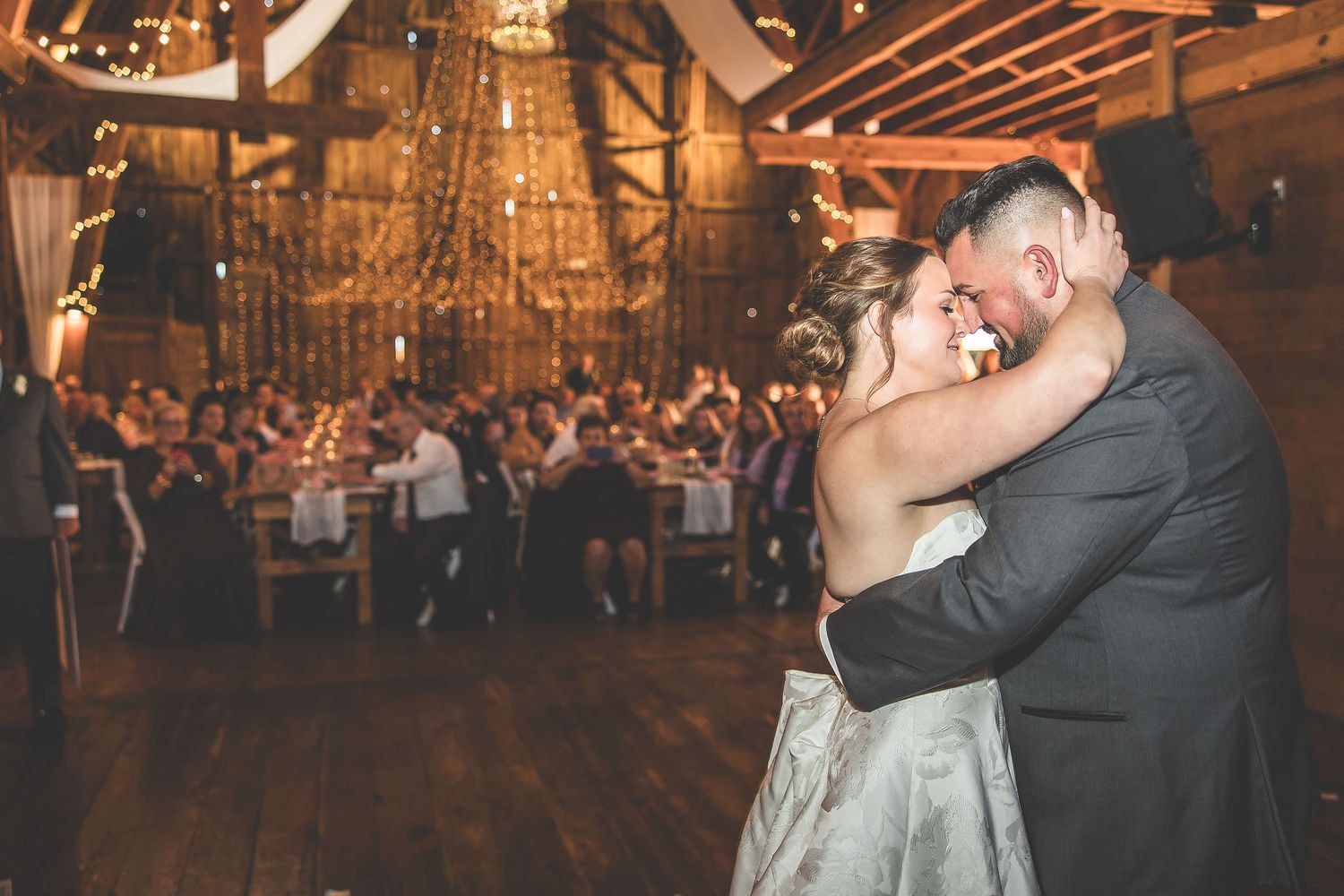 Wedding couple dancing together in a rustic barn venue illuminated by warm lighting and string lights.