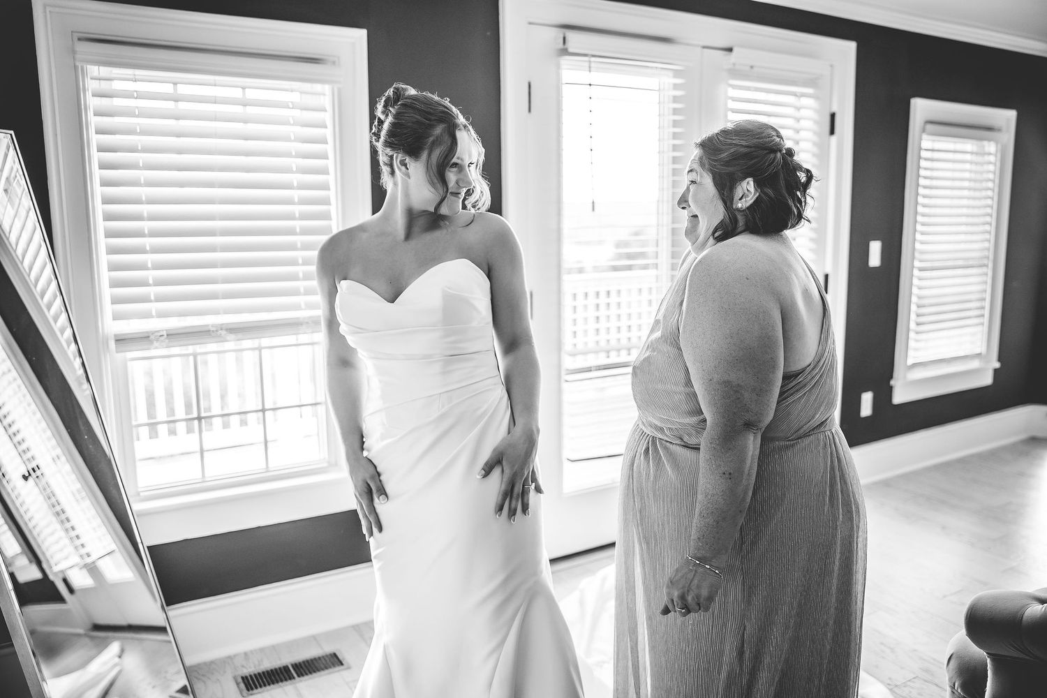 A black and white photo of wedding dress preparations in a room with white shuttered windows.