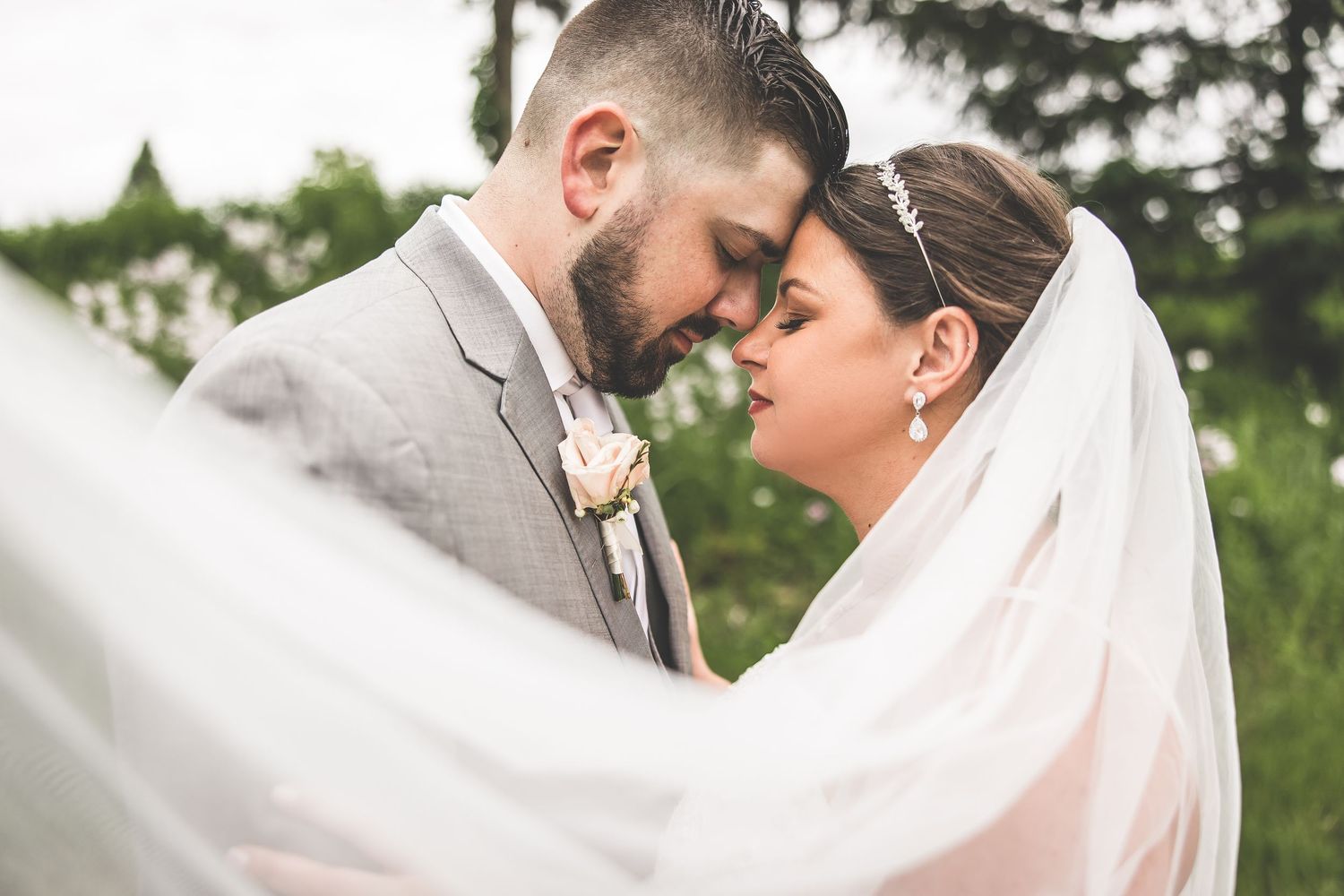 Intimate wedding portrait with flowing veil in soft natural lighting.