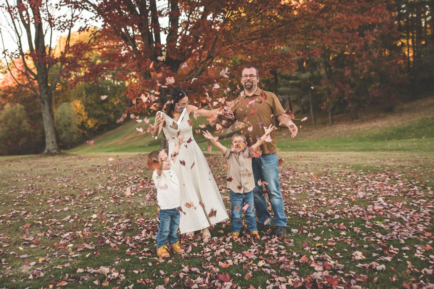 A playful autumn family photoshoot with fallen leaves in a park setting.