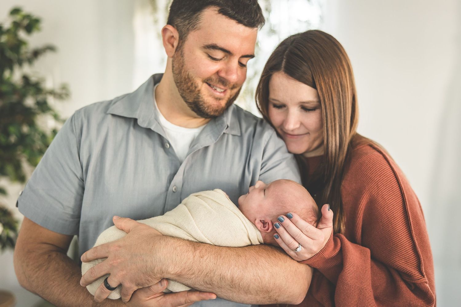 A couple shares an intimate moment with their newborn baby in a bright room.