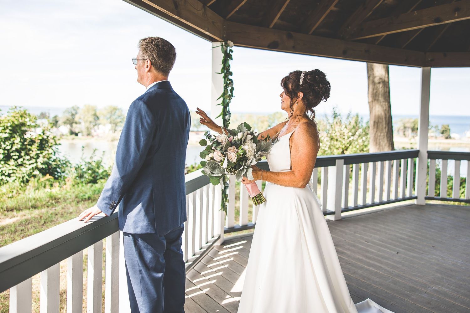 Wedding couple shares an intimate moment on a covered wooden deck with natural lighting.