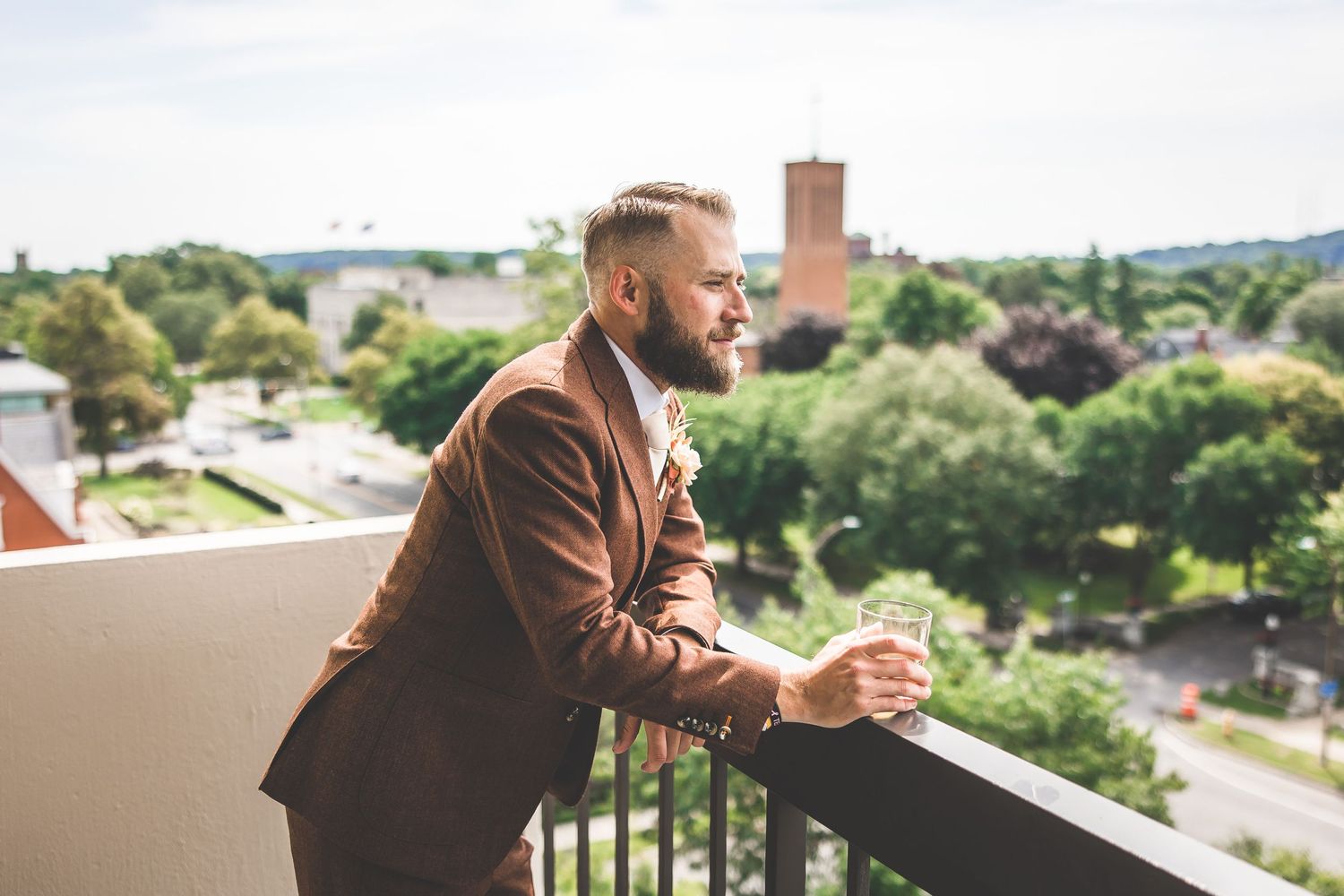 Person in brown blazer standing on balcony overlooking scenic outdoor view.