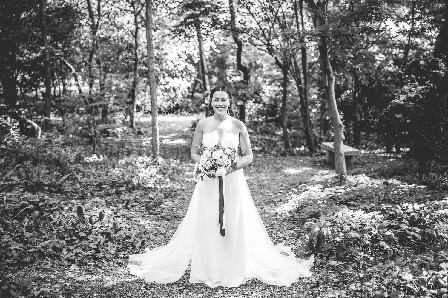 Black and white bridal portrait in wooded garden setting with flowing white dress.