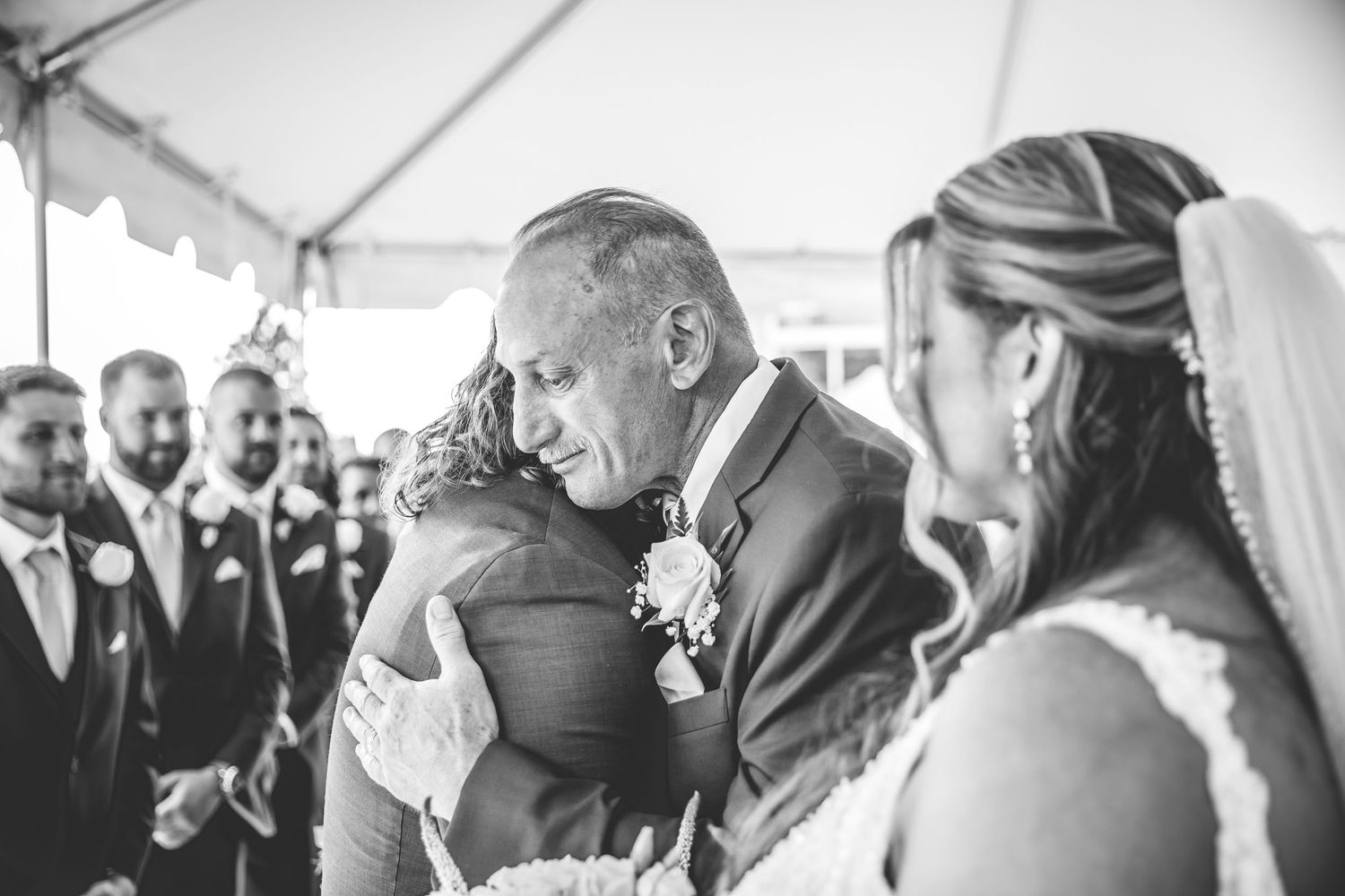 Wedding guests gather under elegant white tent during outdoor ceremony.