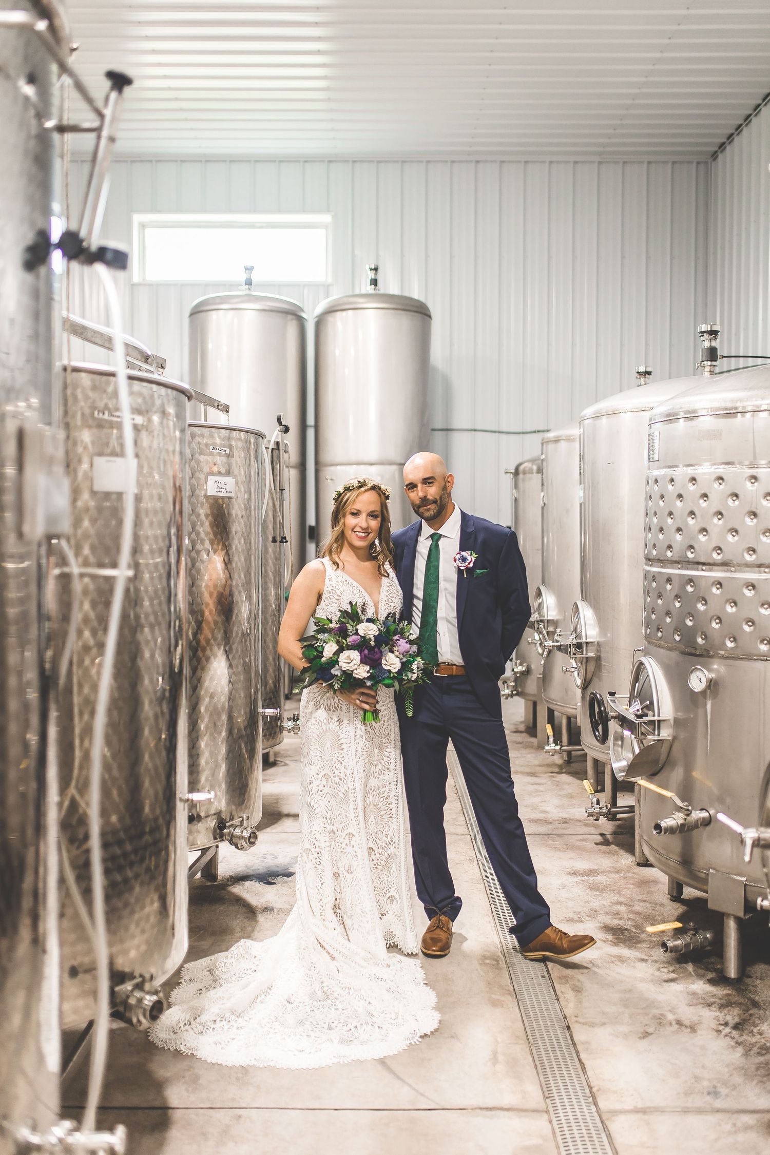 Wedding couple poses together in an industrial winery setting with stainless steel tanks.