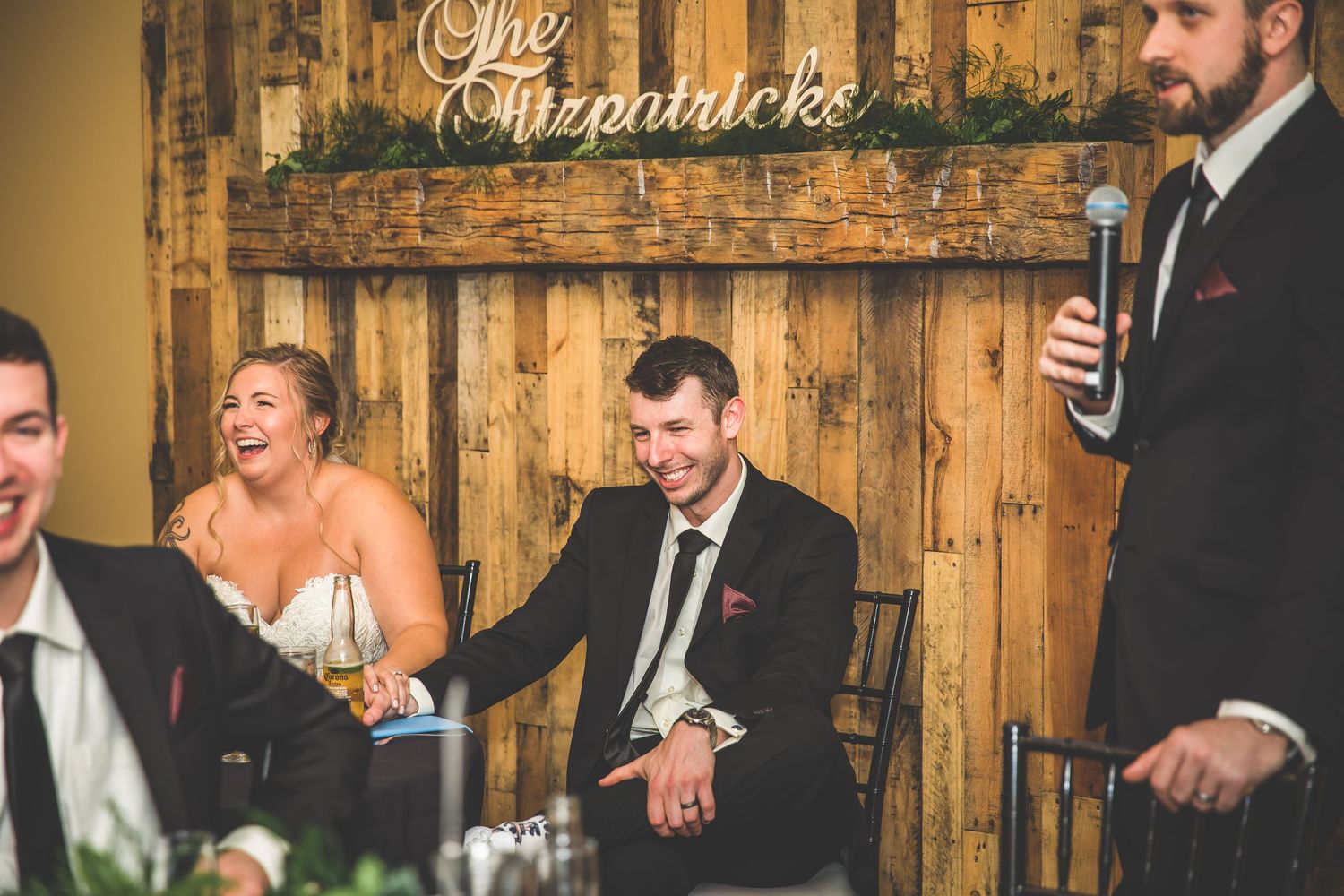 Wedding couple shares playful cake-smashing moment at rustic wooden-walled reception venue.