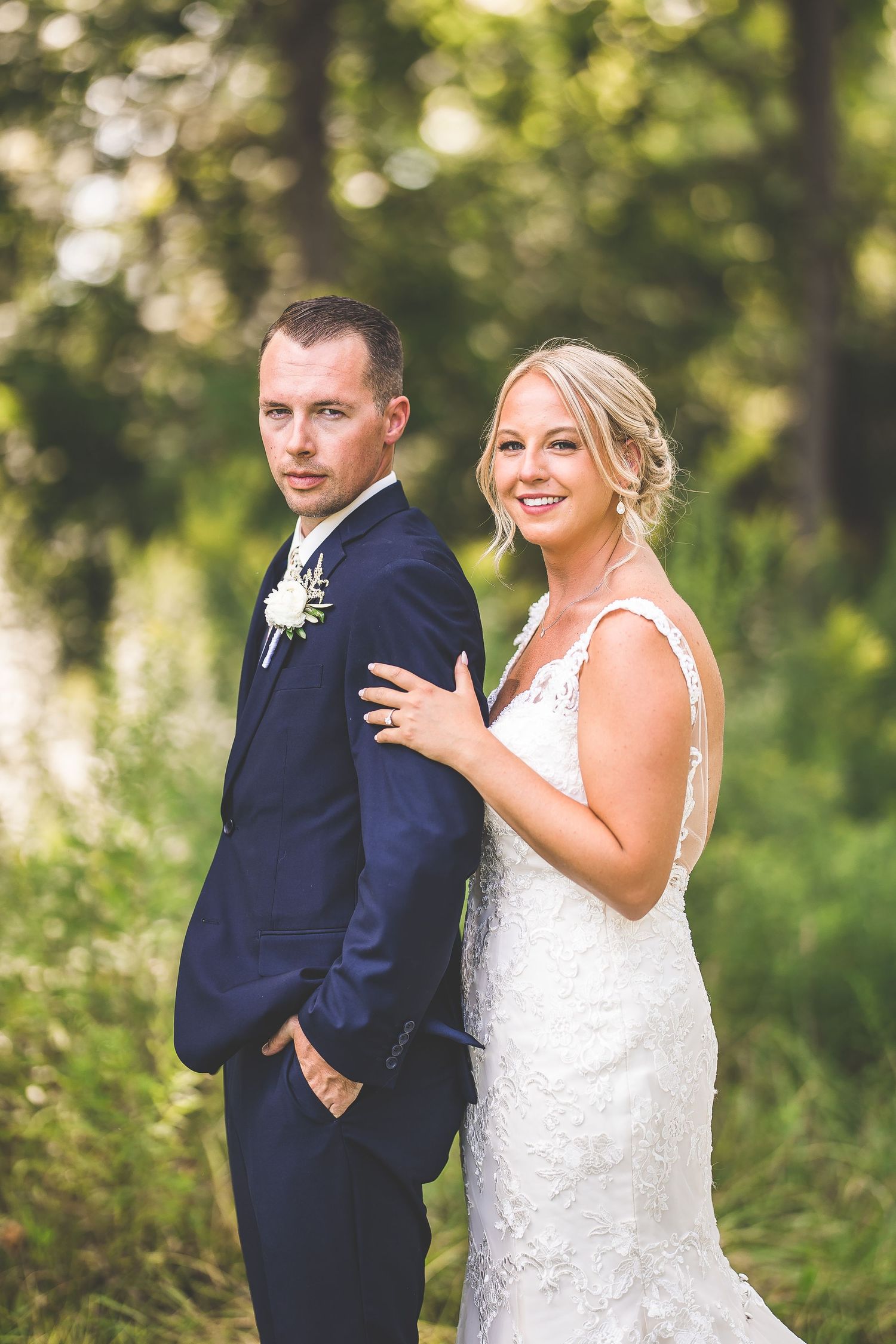 A stylish wedding portrait featuring a couple in formal attire posing in a natural outdoor setting.