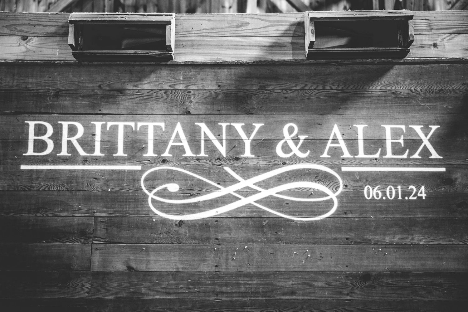 Wedding date and names displayed on rustic wooden barn wall with decorative design.