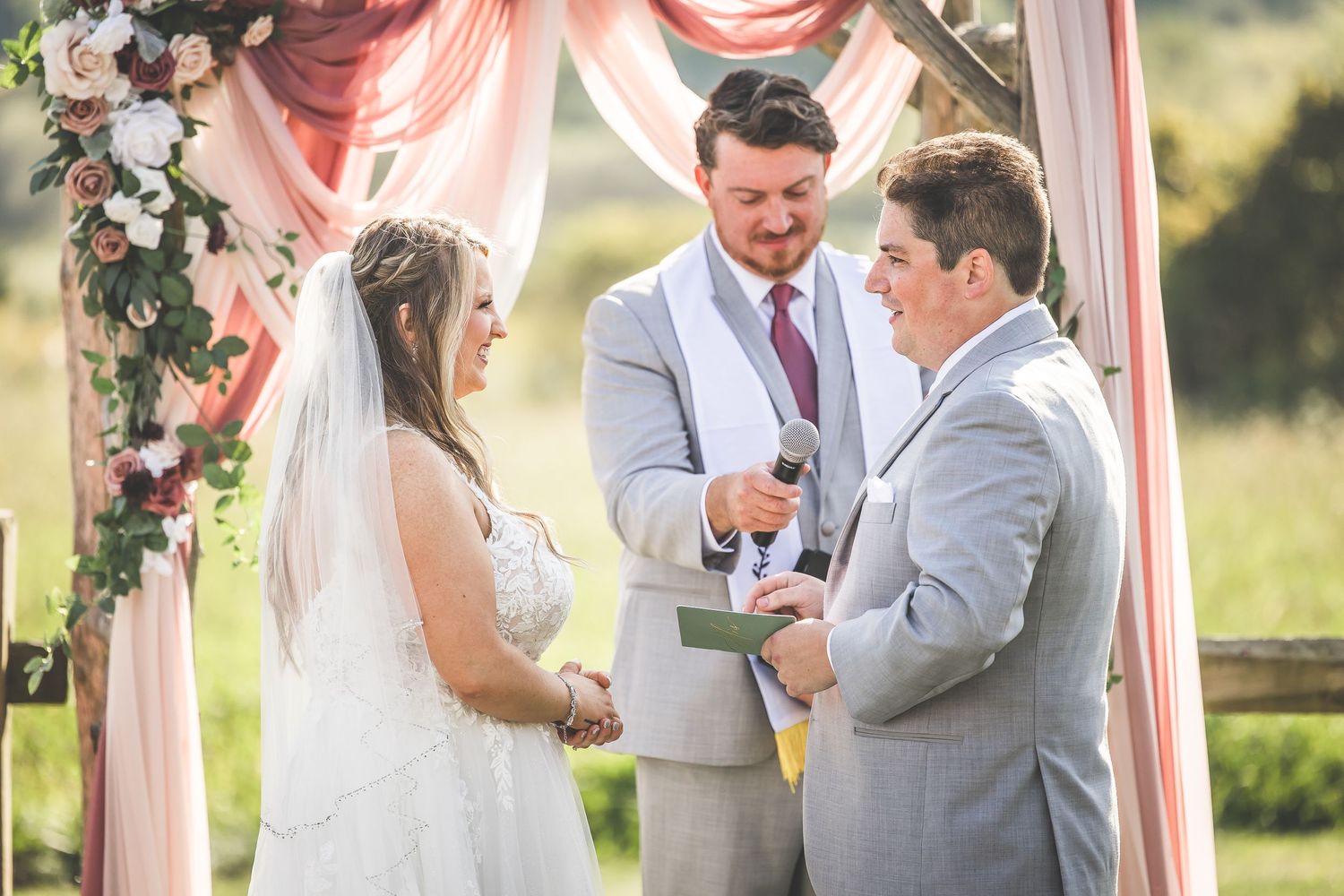 Emotional wedding ceremony moment captured under rustic arch with pink drapery and flowers.