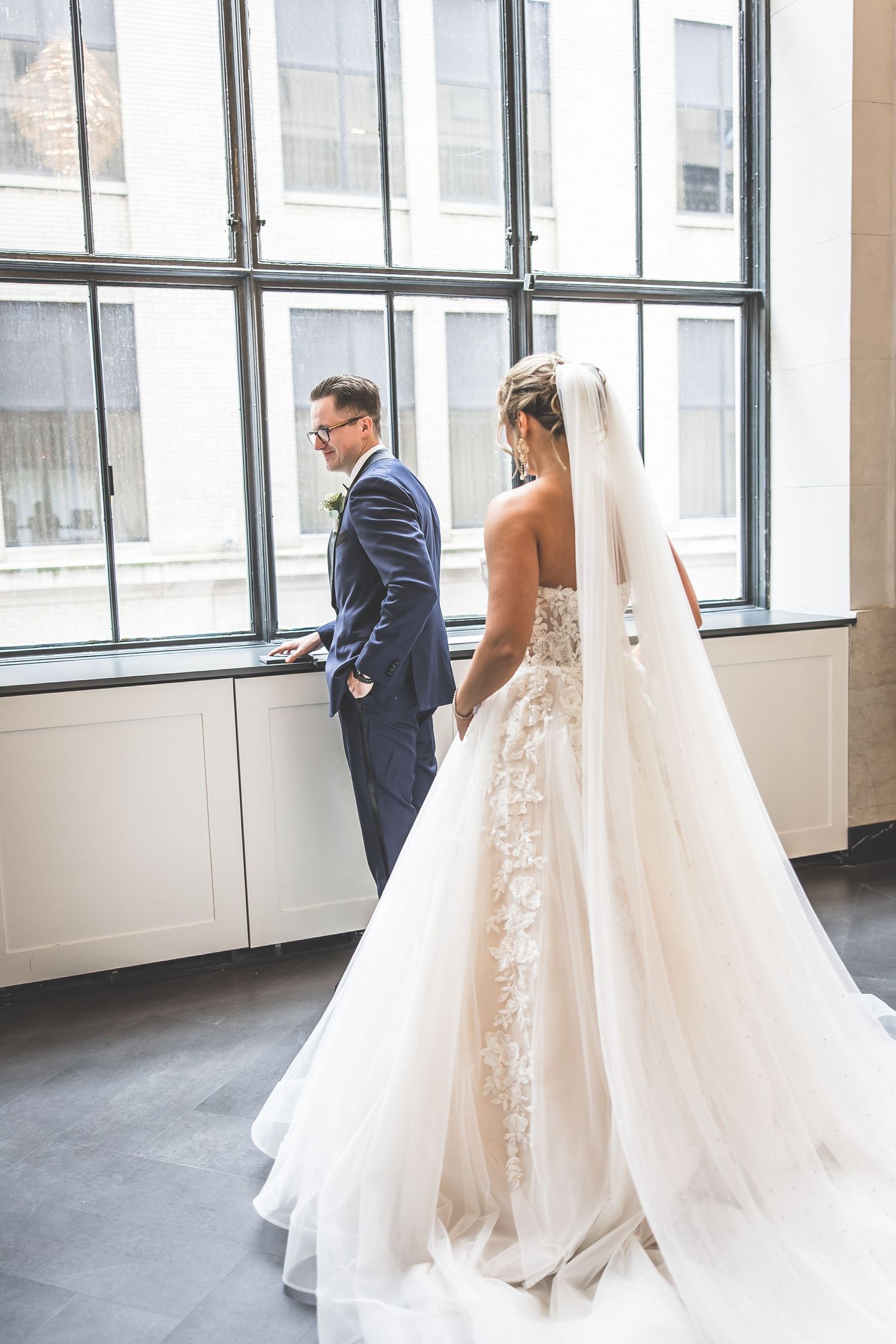 First look wedding moment captured in a bright industrial loft space with large windows.
