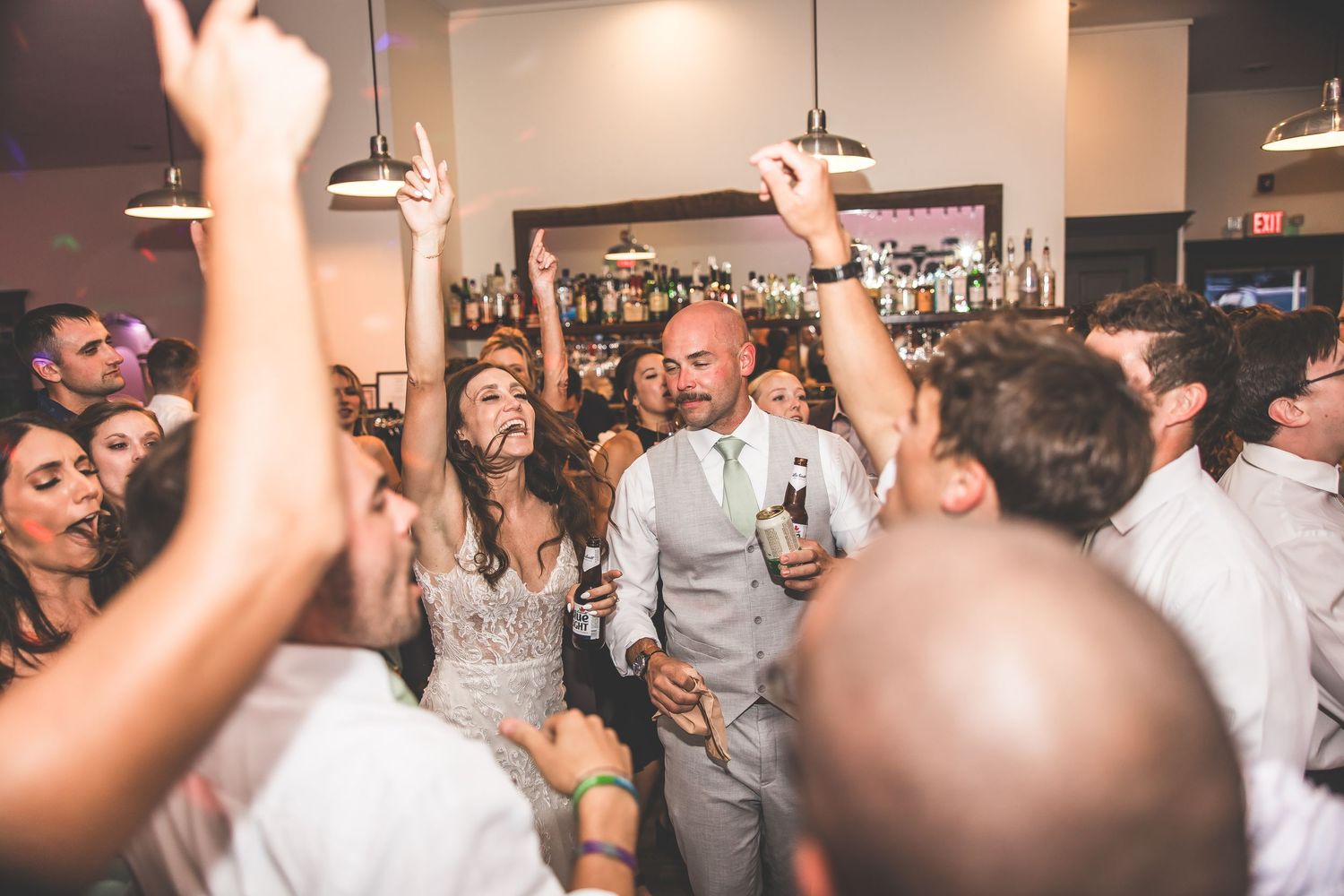 Wedding reception crowd with raised hands dancing and celebrating.