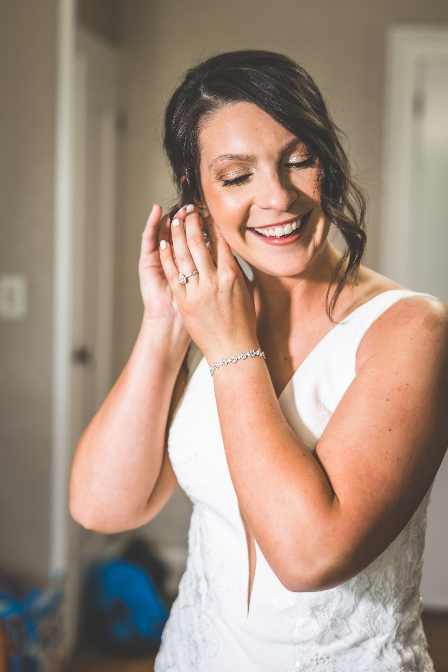 A bride in a white wedding dress smiling and covering her face with her hands.